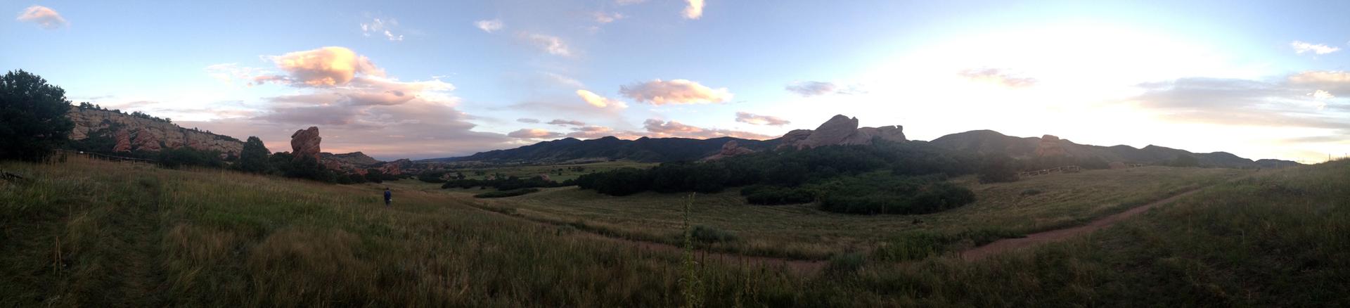 Panoramic view of a grassy valley with mountains under a colorful sunset sky.