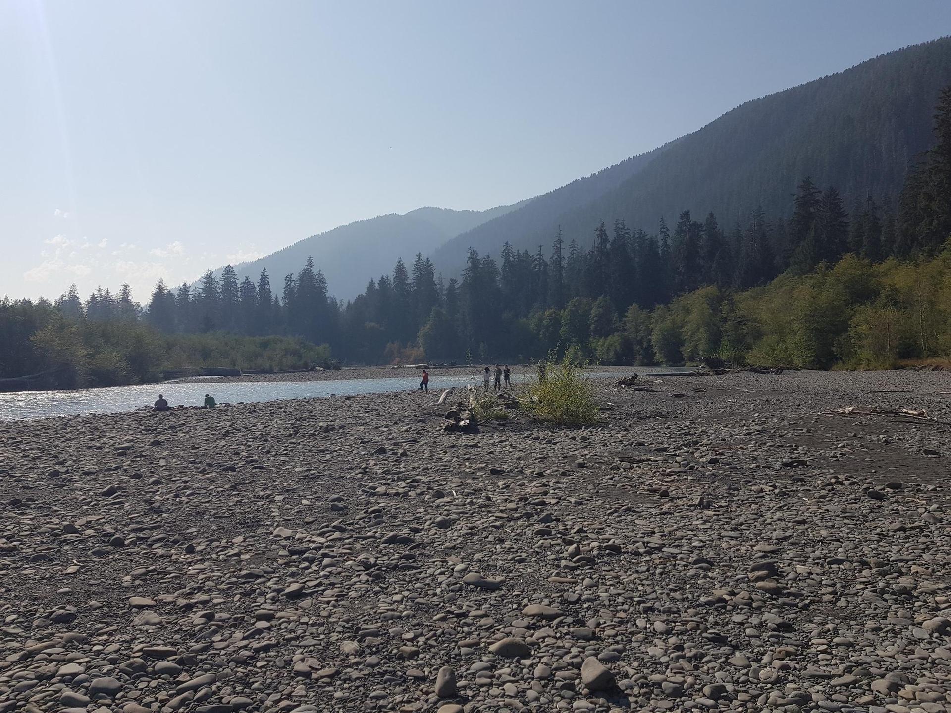 Sunny day on a wide rocky riverbed with distant people and mountains.