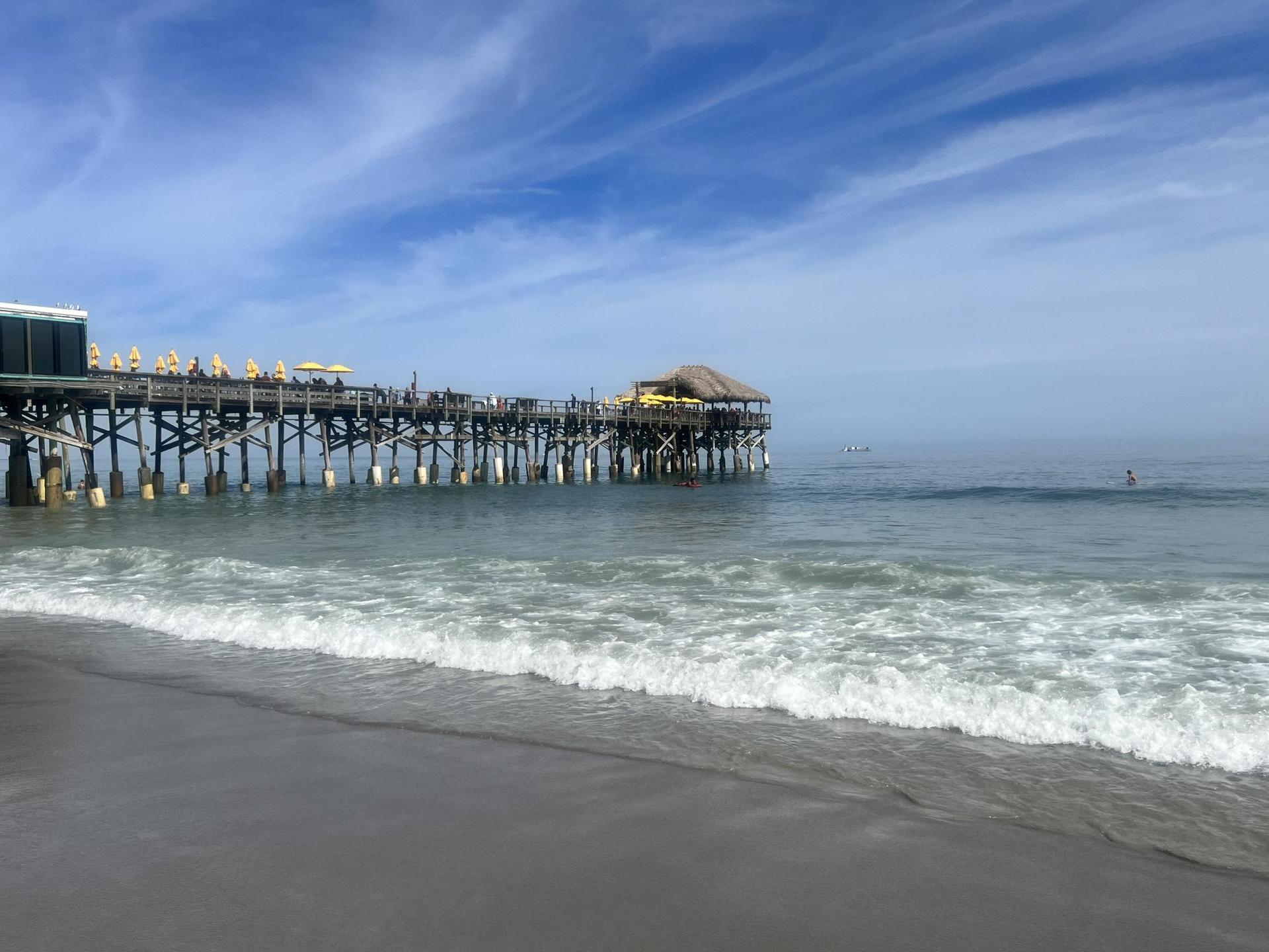 A long wooden pier extends over the ocean under a bright blue sky.