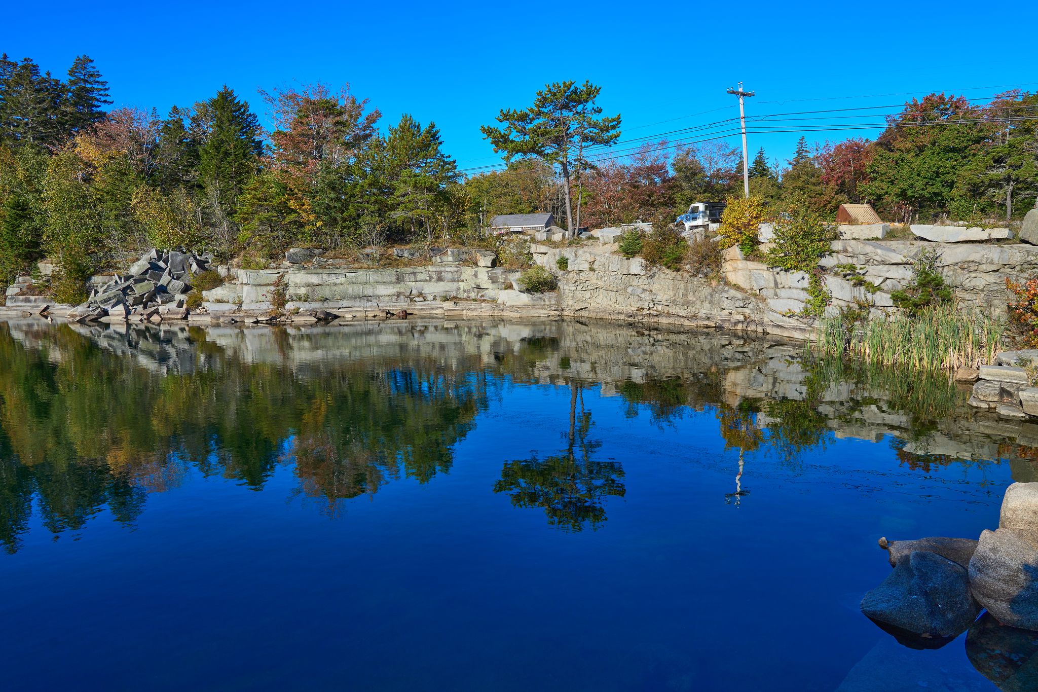 Deep blue quarry pond reflecting surrounding trees and rock walls on a clear day. - Vinalhaven & Lawsons Quarry loop