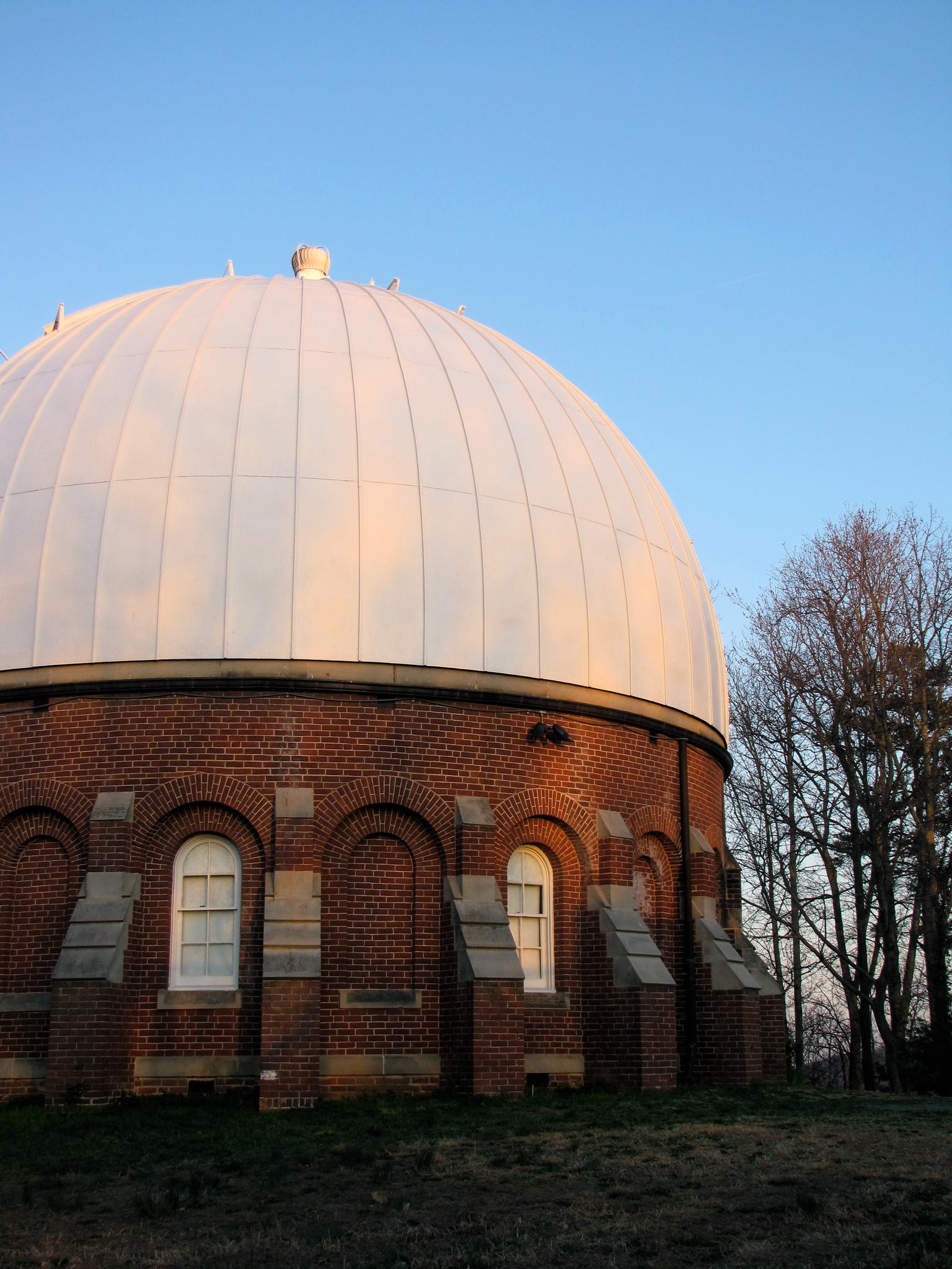 Brick observatory building with a large white dome under a clear blue sky.