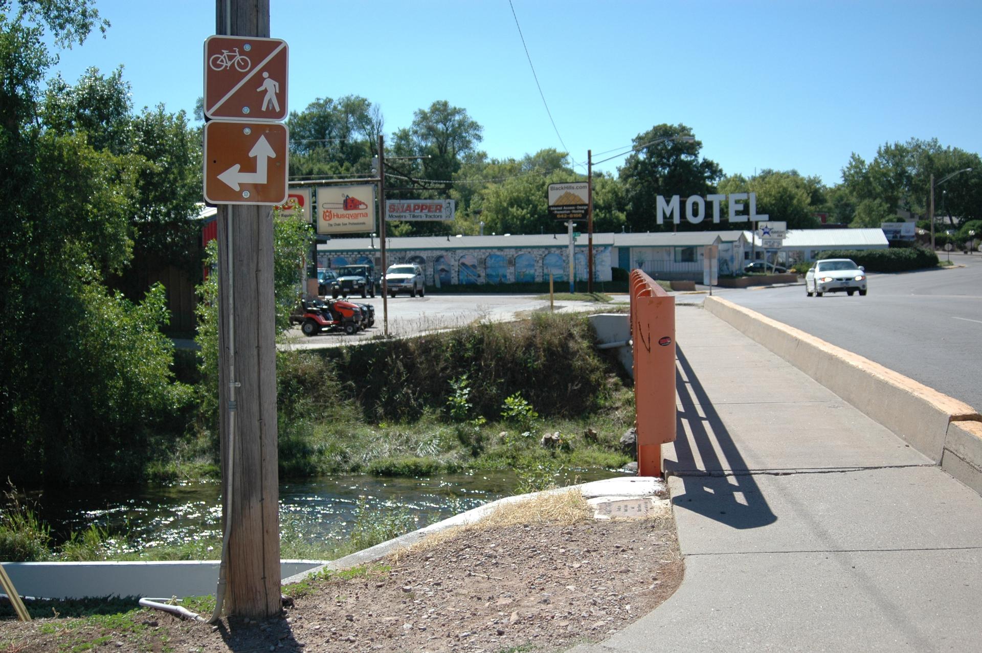 A sunny view of a bridge, river, road, and distant motel.