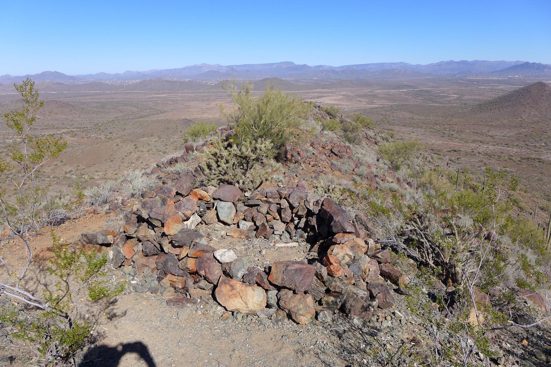 Circular rock structure on a rocky desert hill with distant mountains, bright daylight.