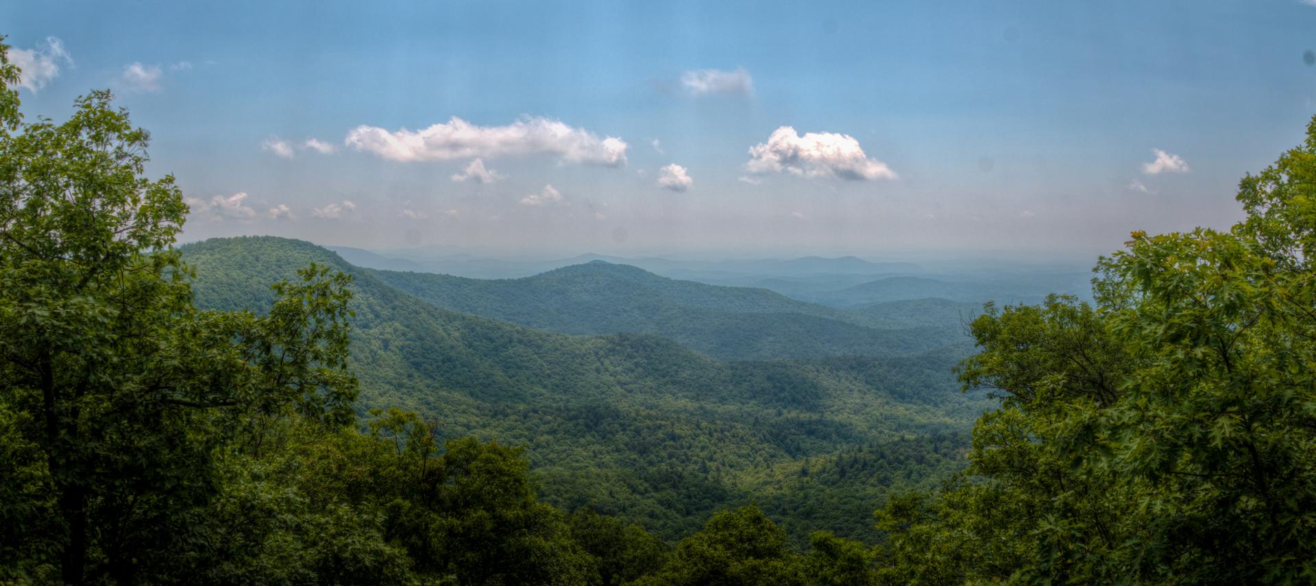 Panoramic view of lush green mountains under a blue sky with white clouds.