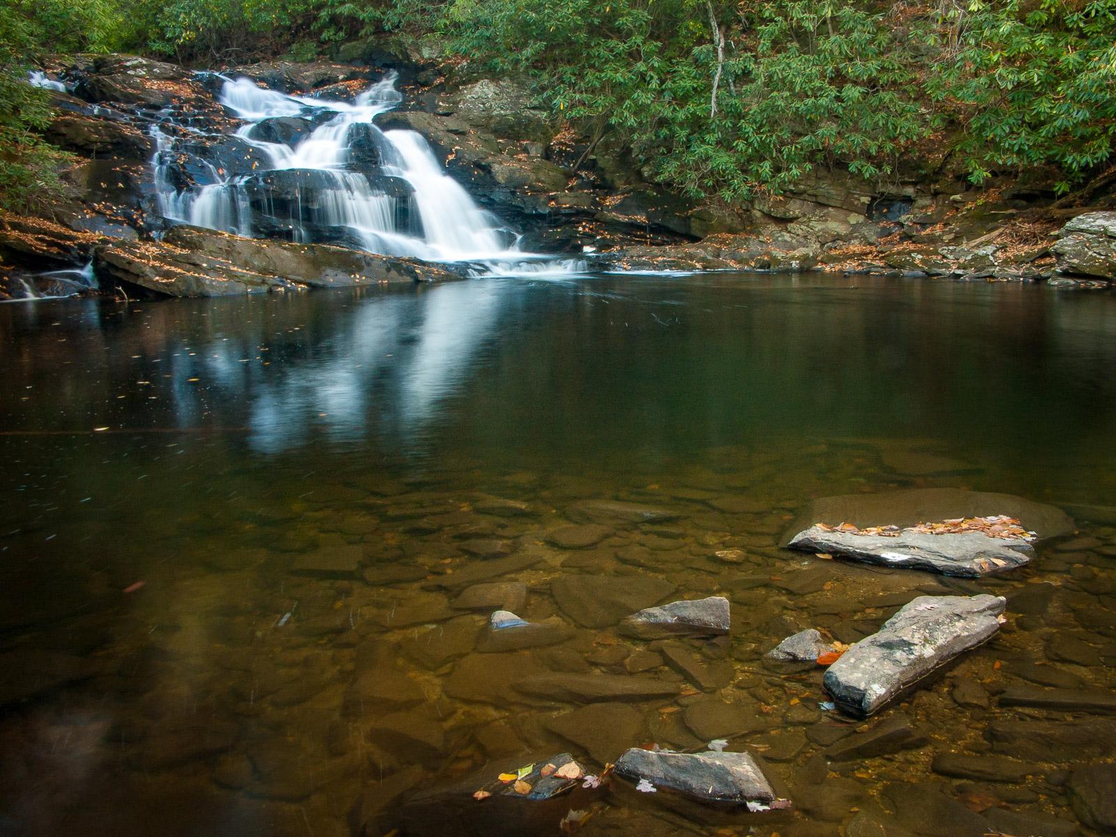 A waterfall cascades into a clear, dark pool surrounded by green forest.