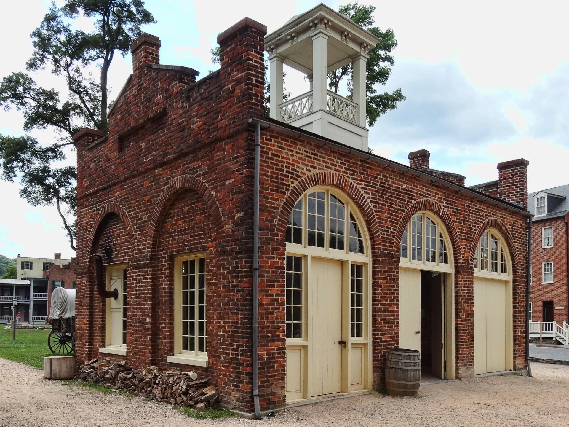 Old brick building with arched windows and cupola under cloudy sky.