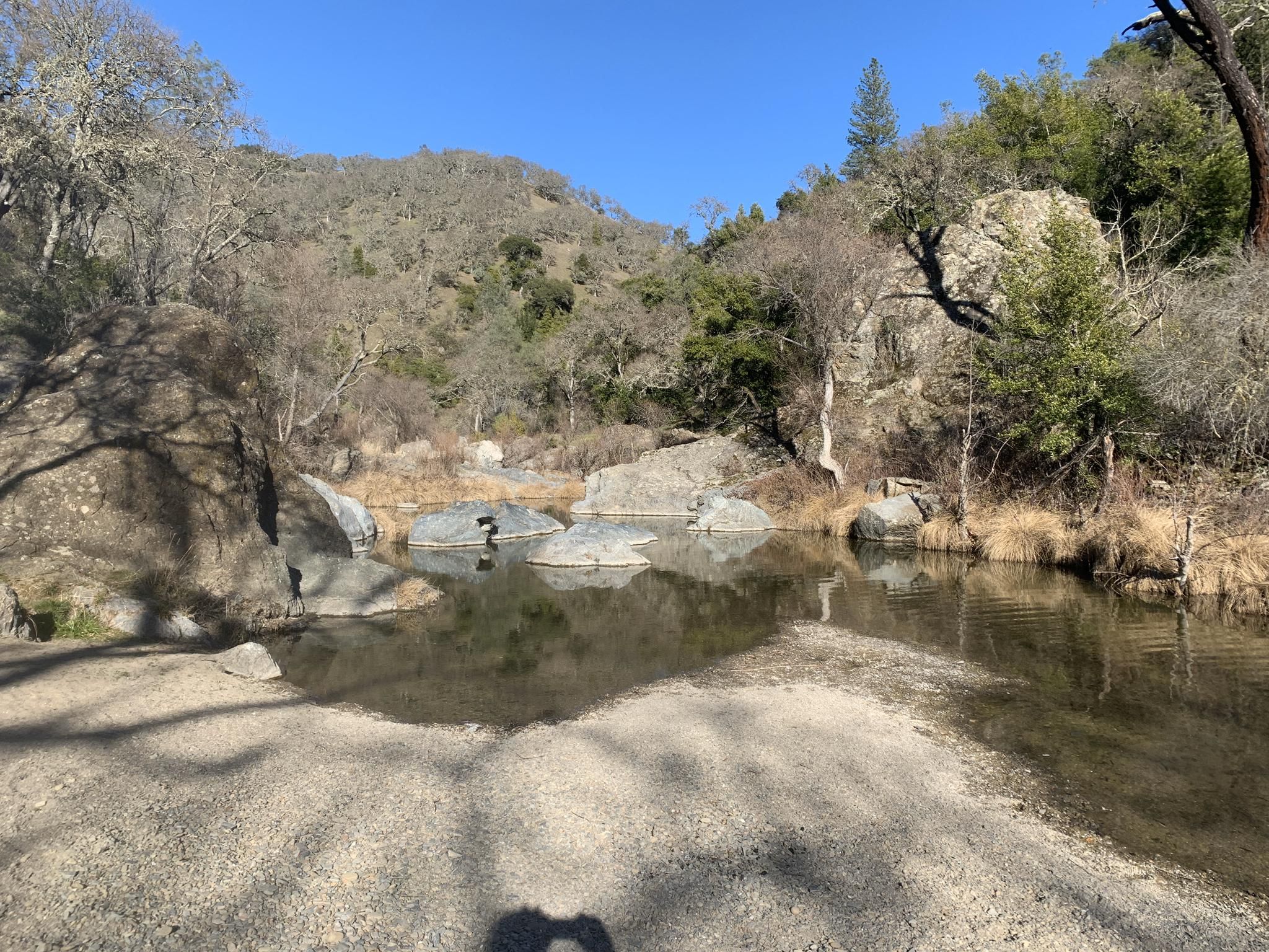 Calm river with large rocks, surrounded by hills and bare trees. - China Hole Loop