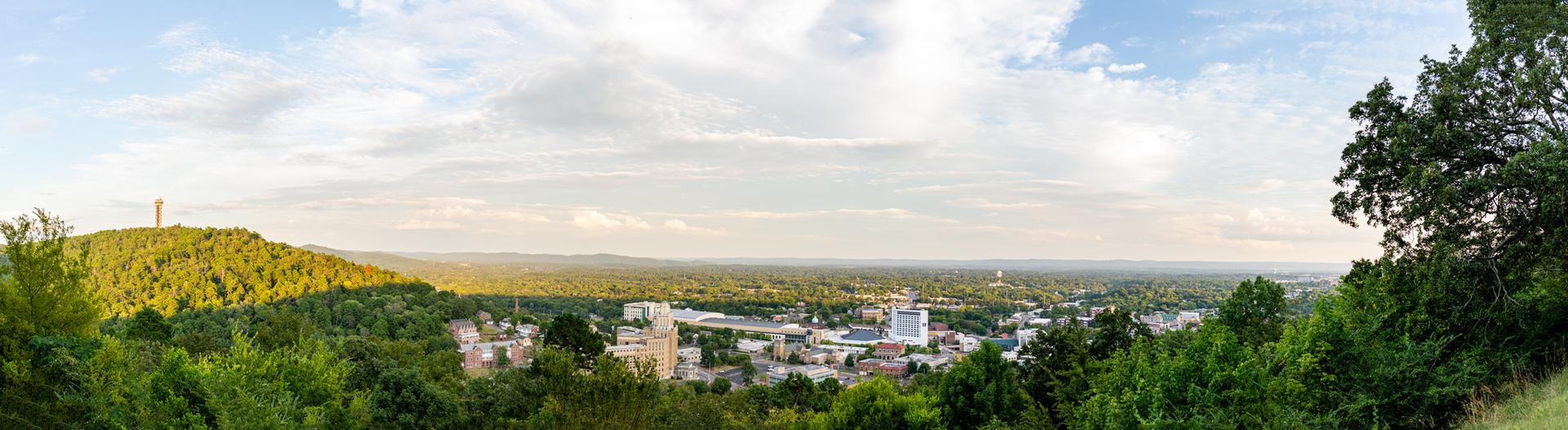 Panoramic view of a town surrounded by green hills under a cloudy sky.
