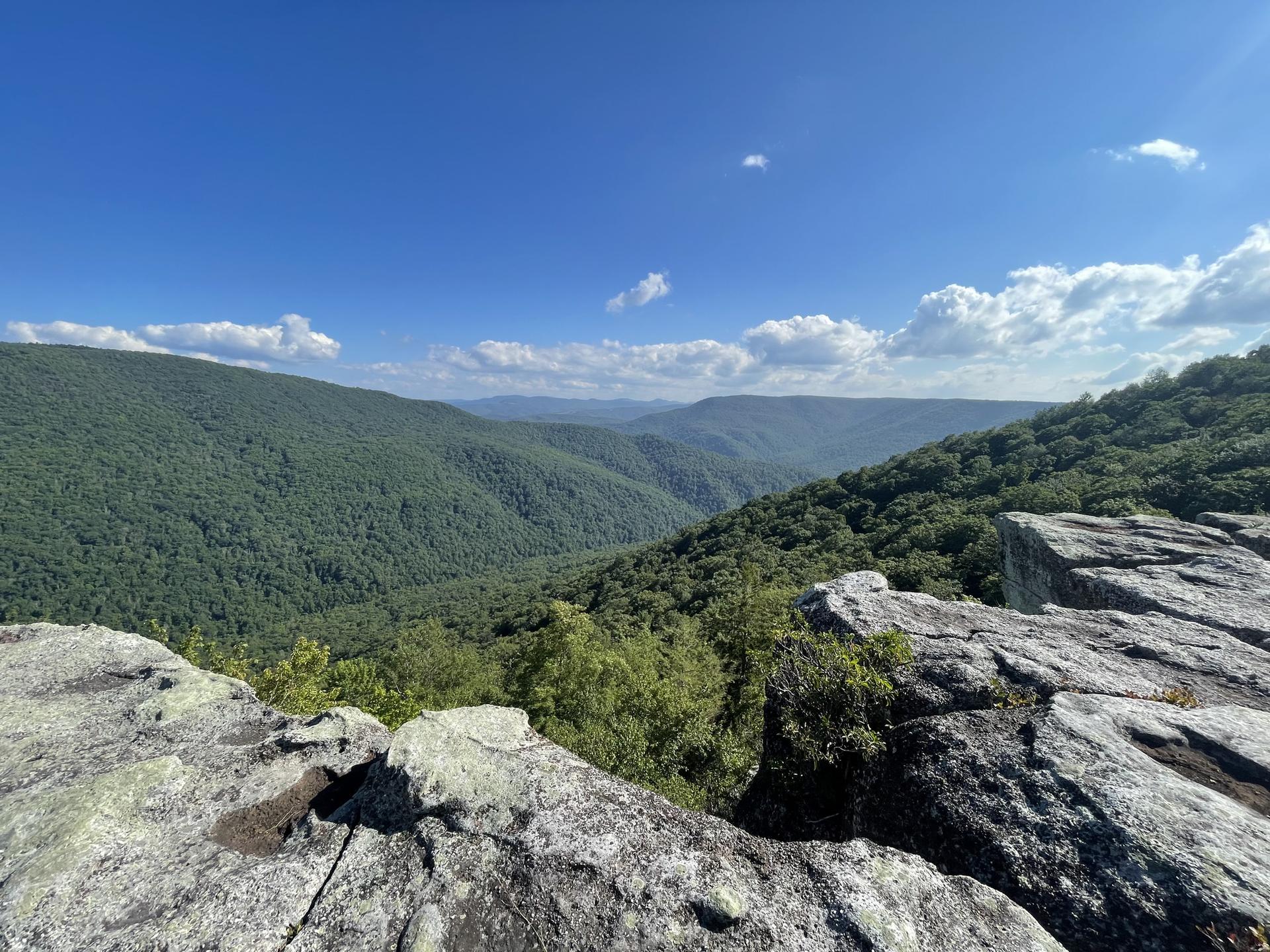 Sunny view of vast green mountains and valleys from a rocky overlook.
