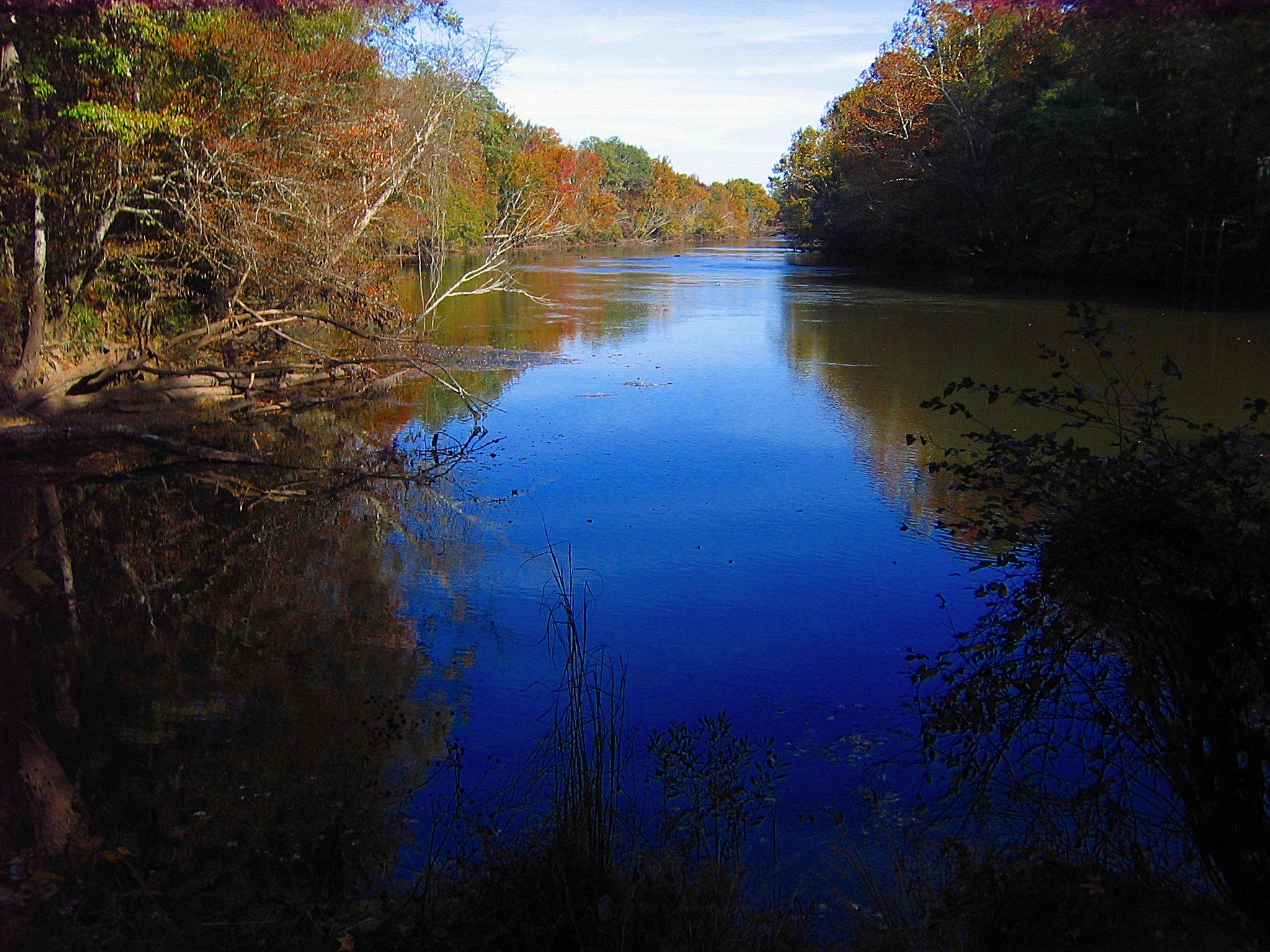 Calm river reflecting blue sky, surrounded by colorful autumn trees.