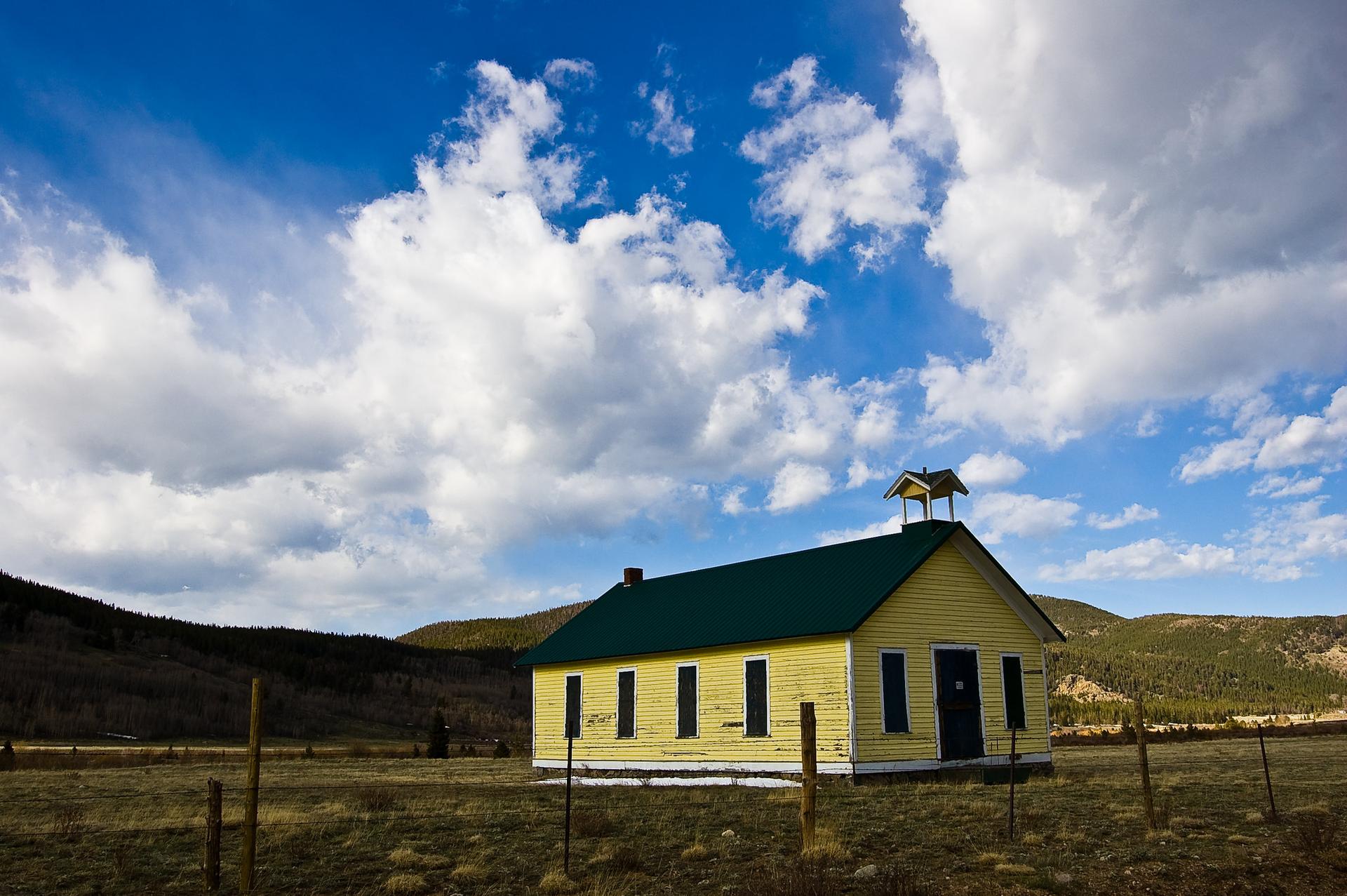 Yellow building with green roof in a sunny field under a cloudy blue sky.