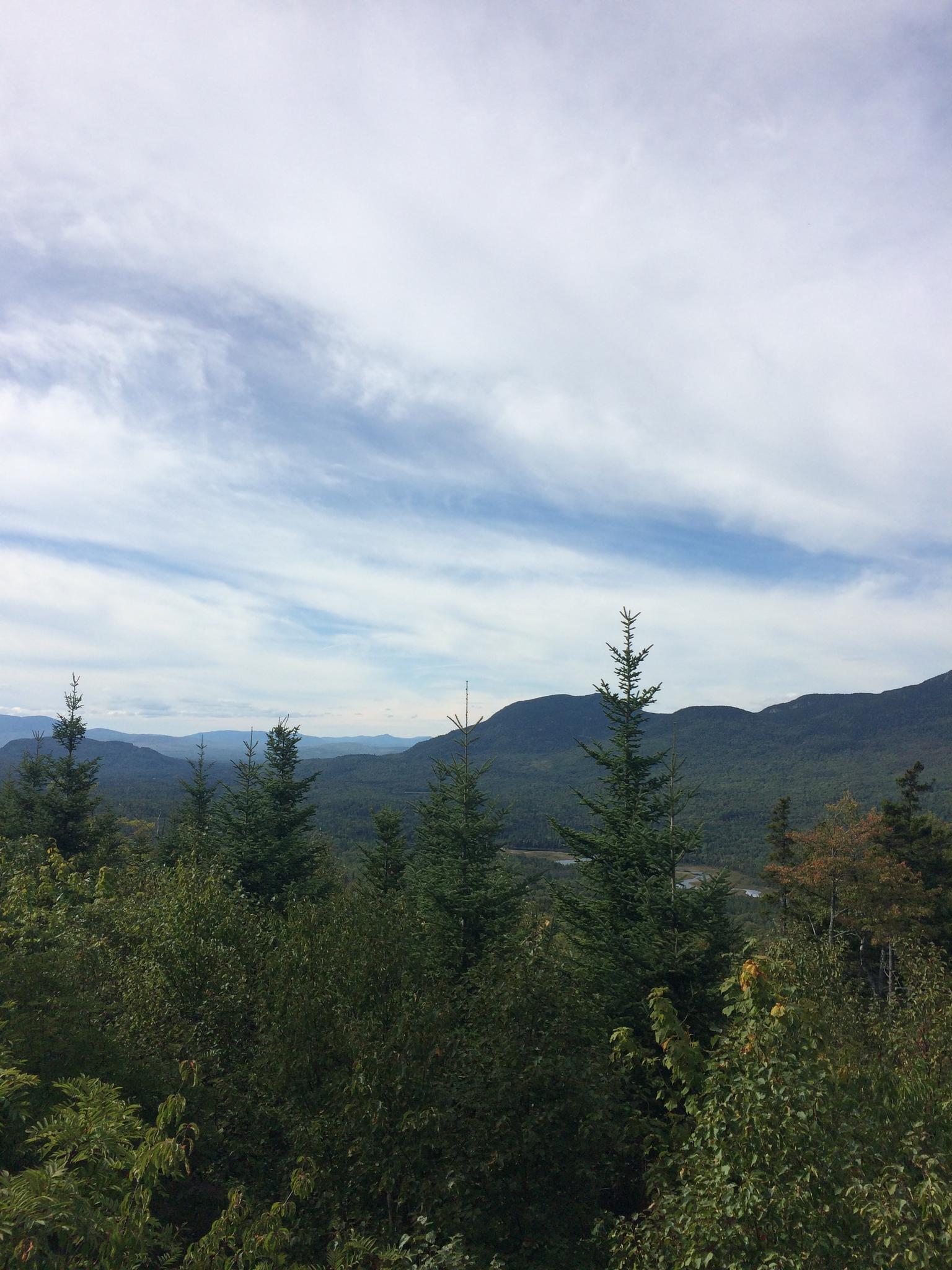 Expansive view of green forested mountains under a cloudy blue sky.