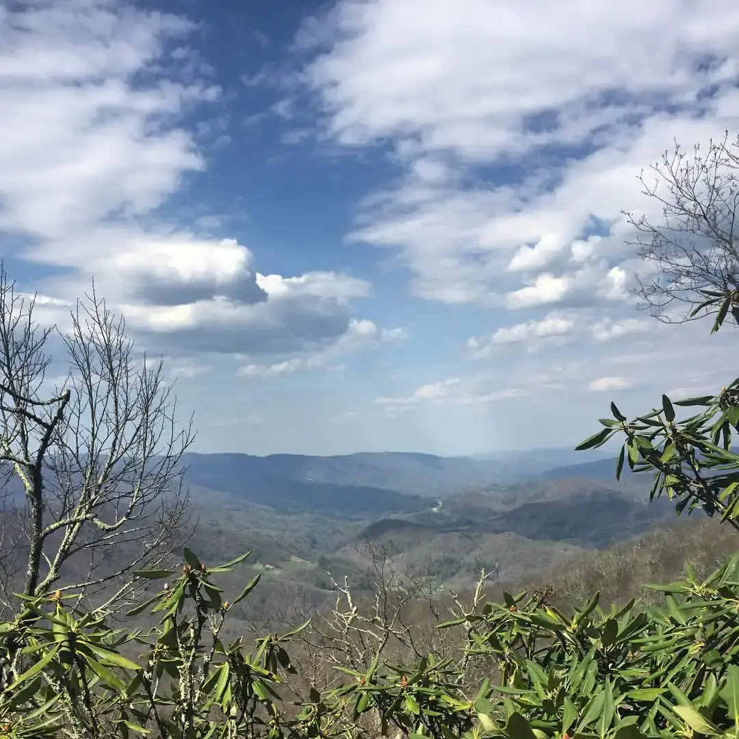 Expansive mountain vista with scattered clouds and foreground foliage.