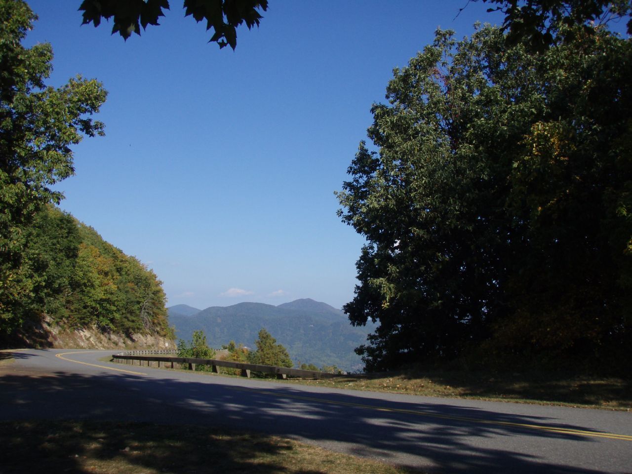 Winding mountain road with guardrail, framed by trees, under clear blue sky. - Roanoke River Overlook to Mills Gap Overlook
