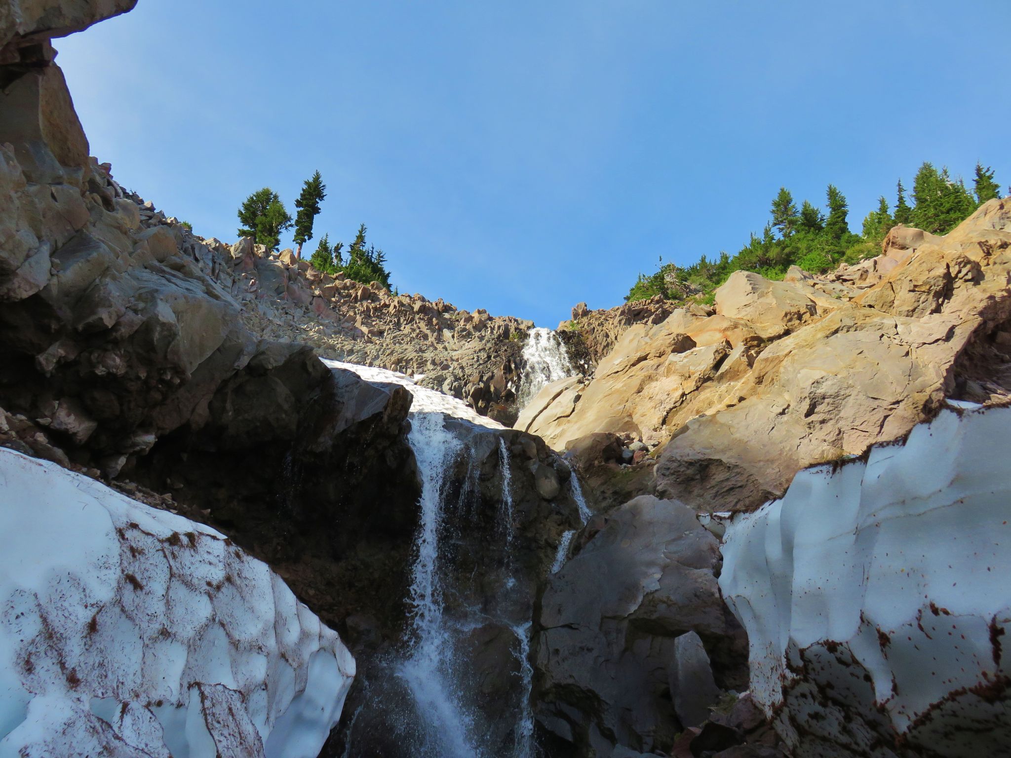 Waterfall cascades over rocky terrain and snow under a bright blue sky. - Cloud Cap to Elk Cove