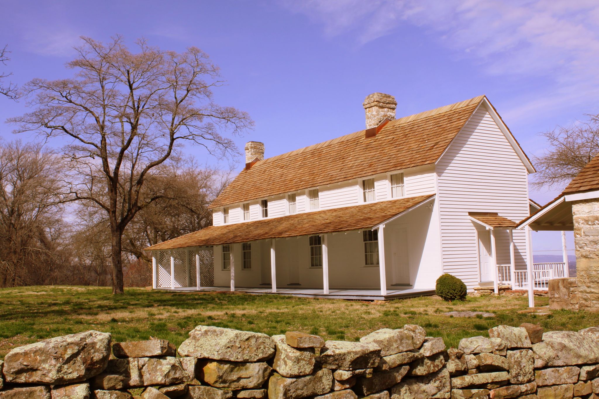 White historic house with a long porch and stone wall under blue sky. - Mountain Beautiful and Hardy Trail Loop