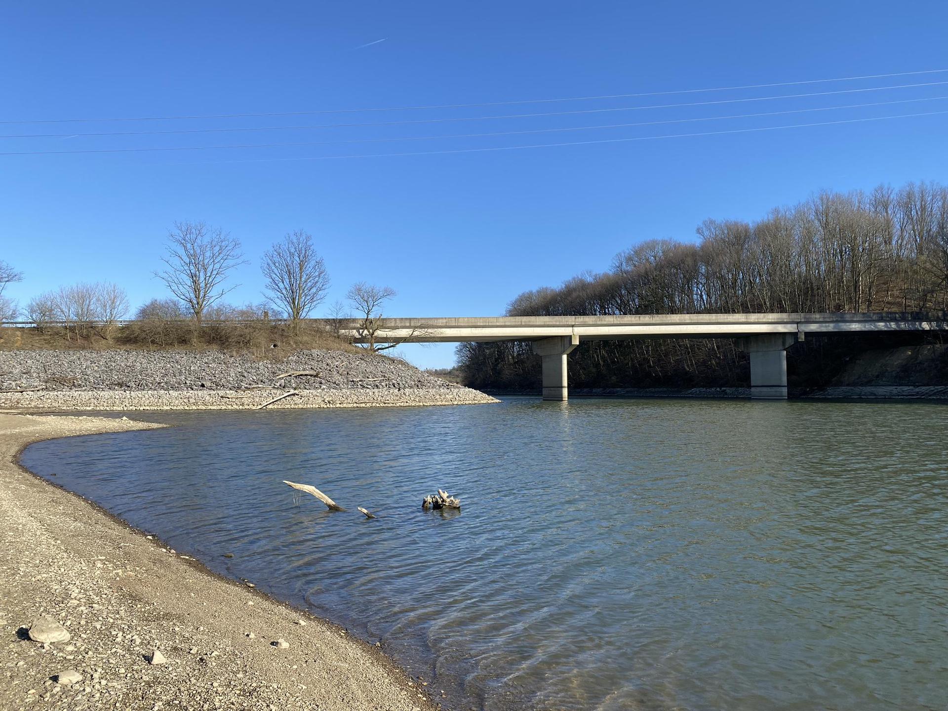 A wide river with a concrete bridge in the distance under clear blue sky.