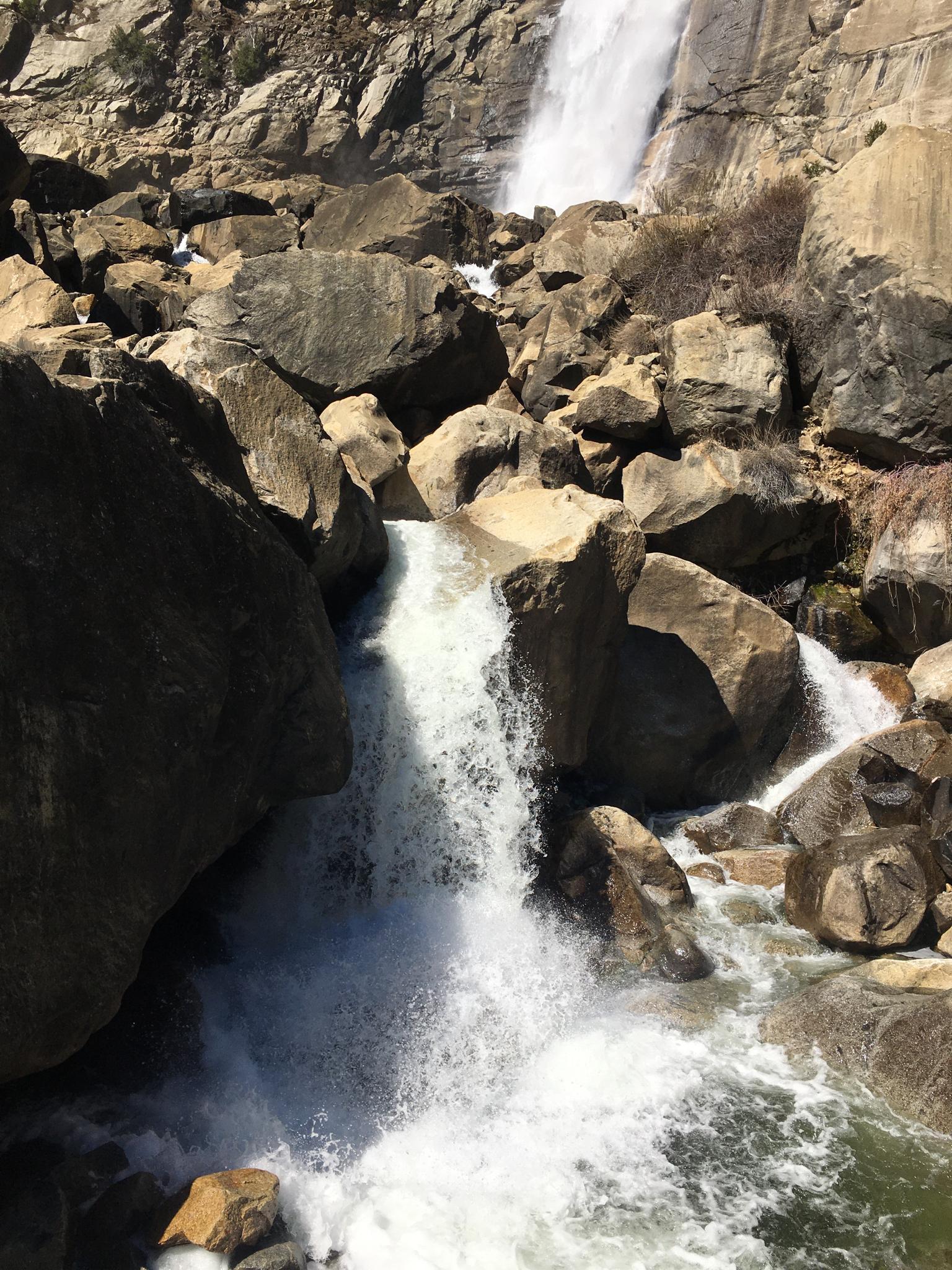 Powerful waterfall cascading over large rocks, creating mist in bright sunlight.