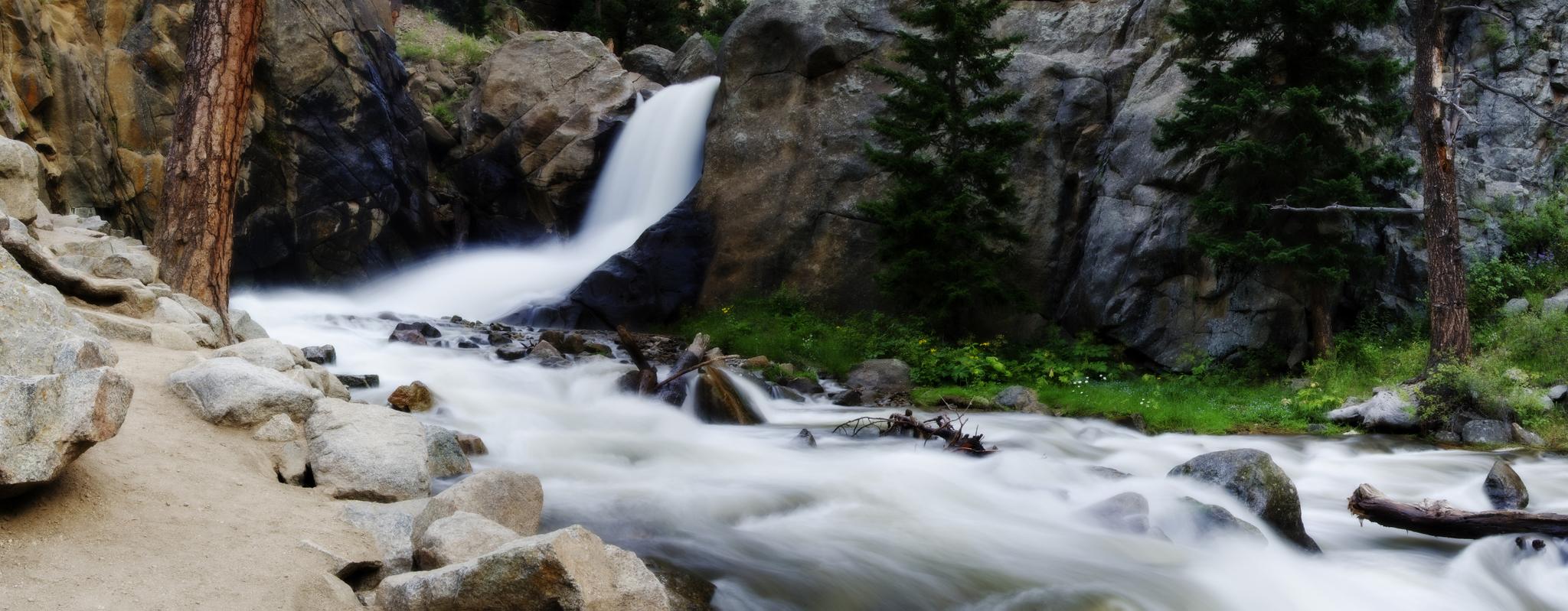 Long exposure waterfall and river flowing through a rocky, forested landscape.