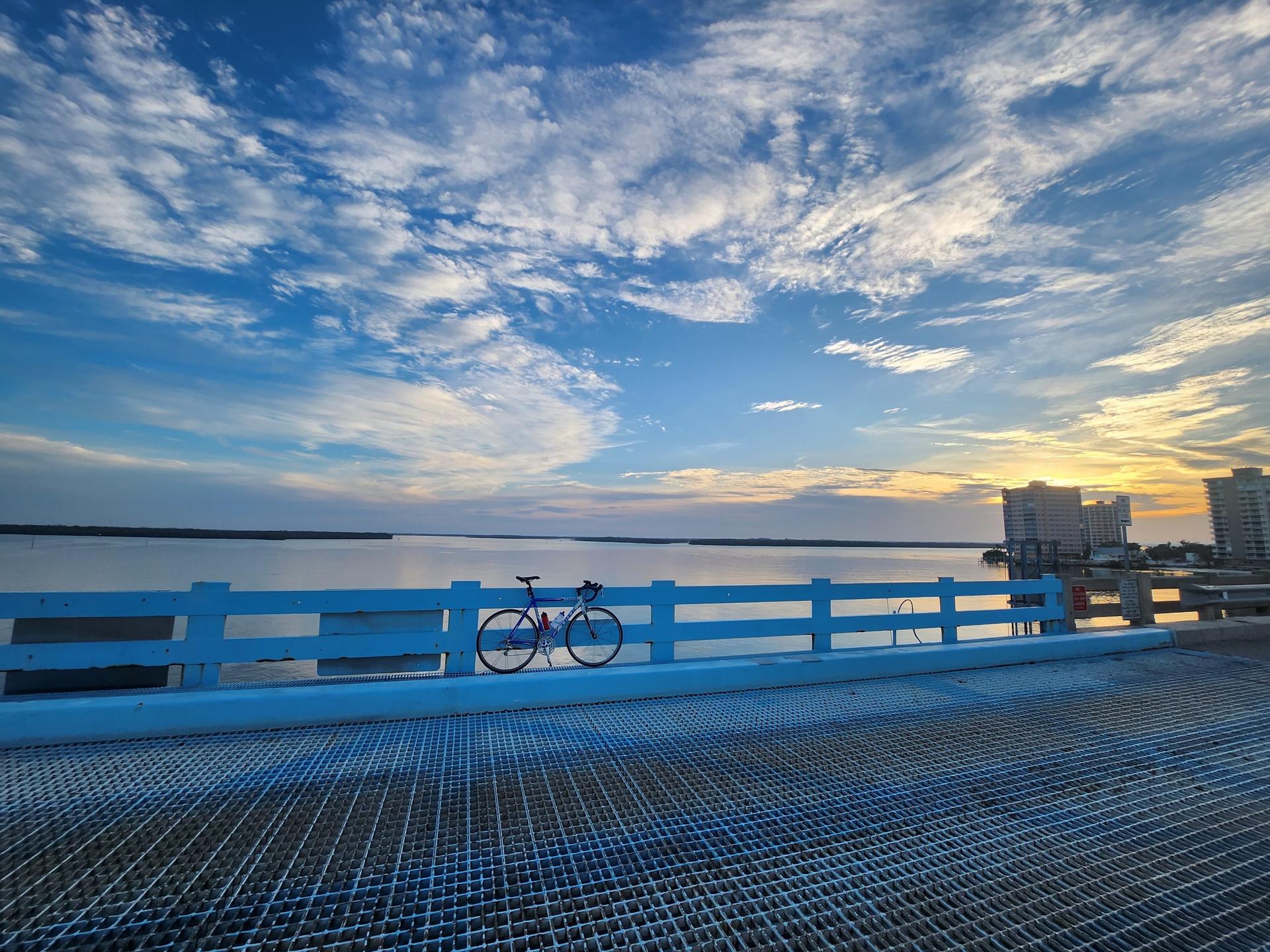 Bicycle on a bridge railing overlooking a wide bay at sunset.