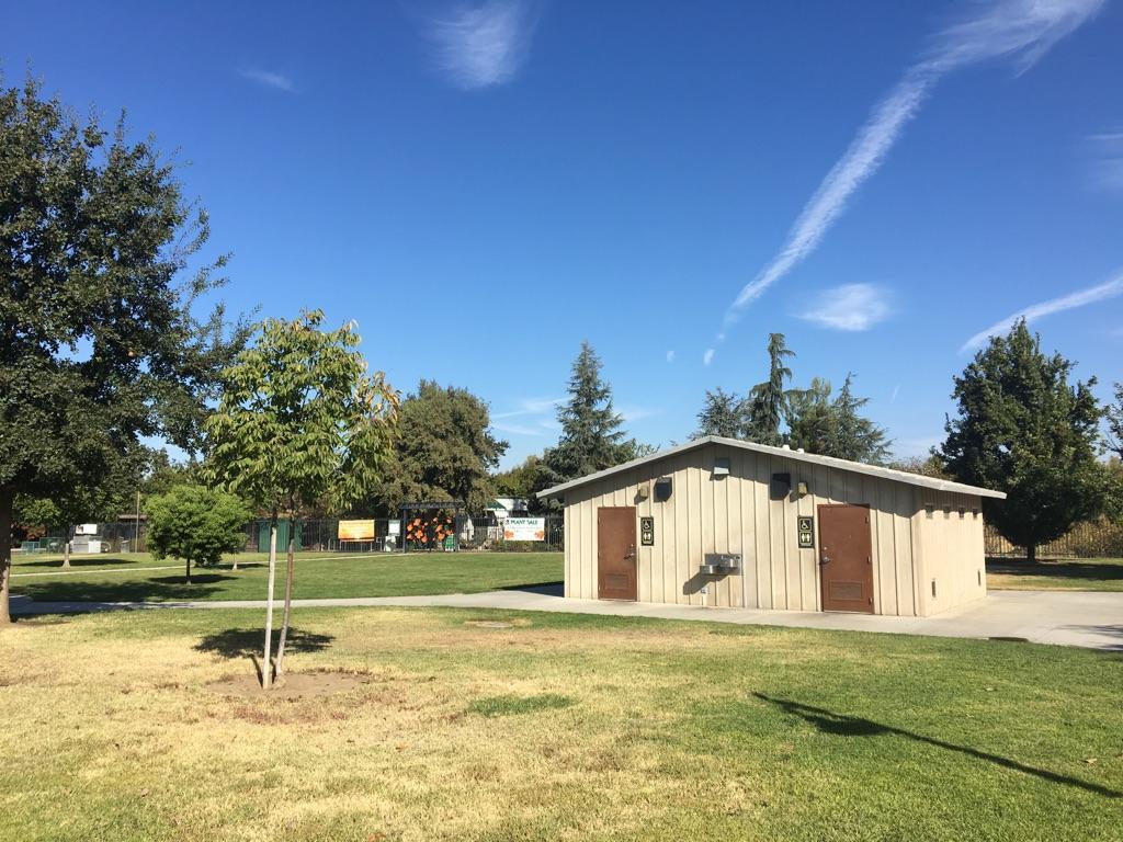 Small utility building in a sunny, grassy park with trees and blue sky.
