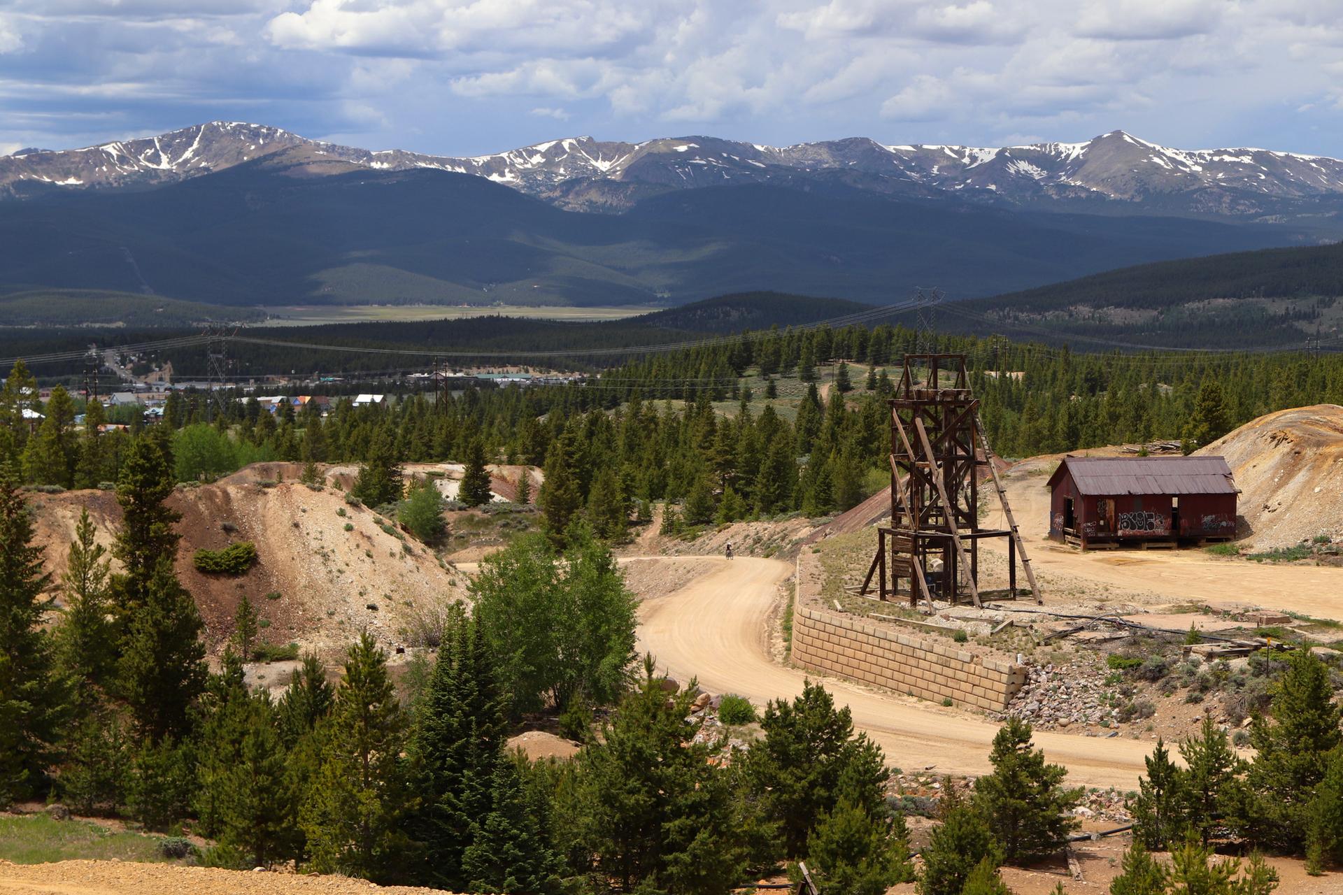 Old mining structure and building in a forested mountain landscape under cloudy skies.