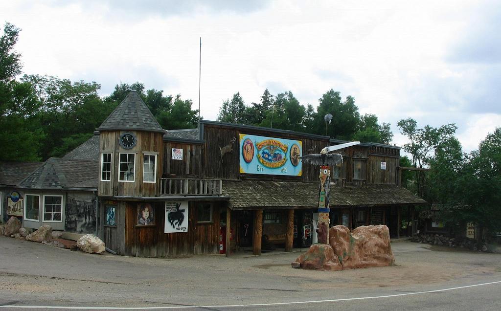 Rustic wooden building with signs and a totem pole under a cloudy sky.