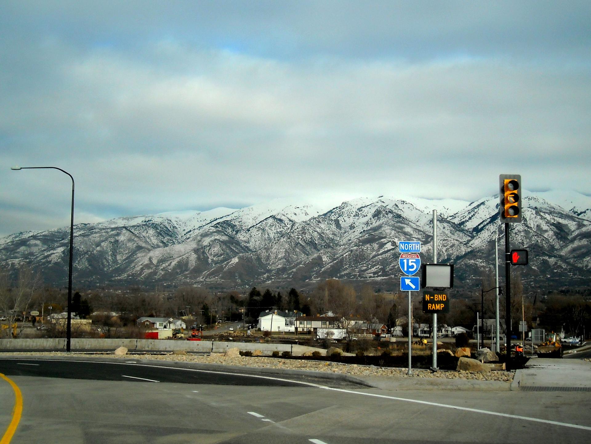 Road intersection with traffic lights and snow-capped mountains under a cloudy sky.