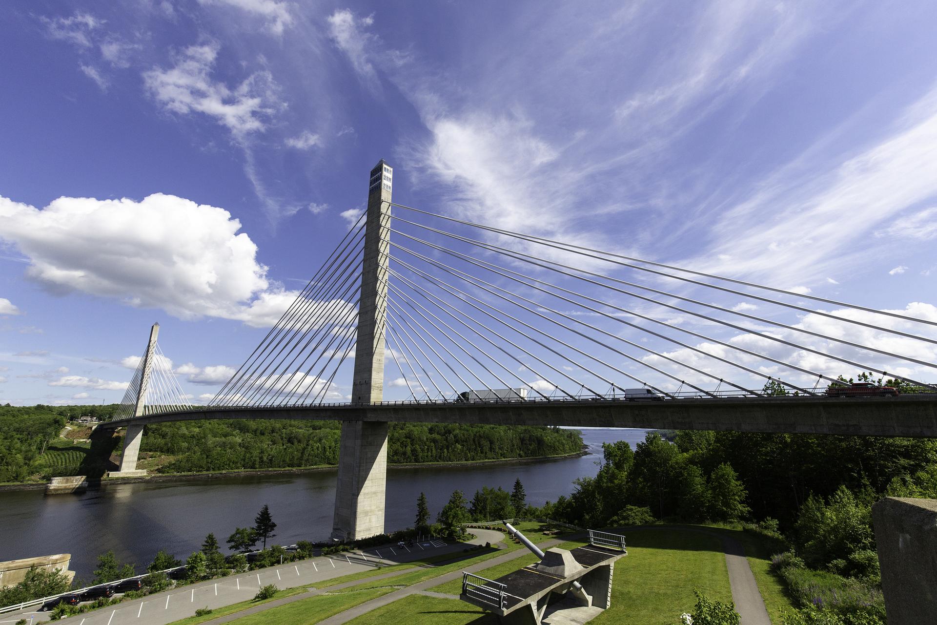 Majestic cable-stayed bridge spans a river with forested banks under a bright blue sky.