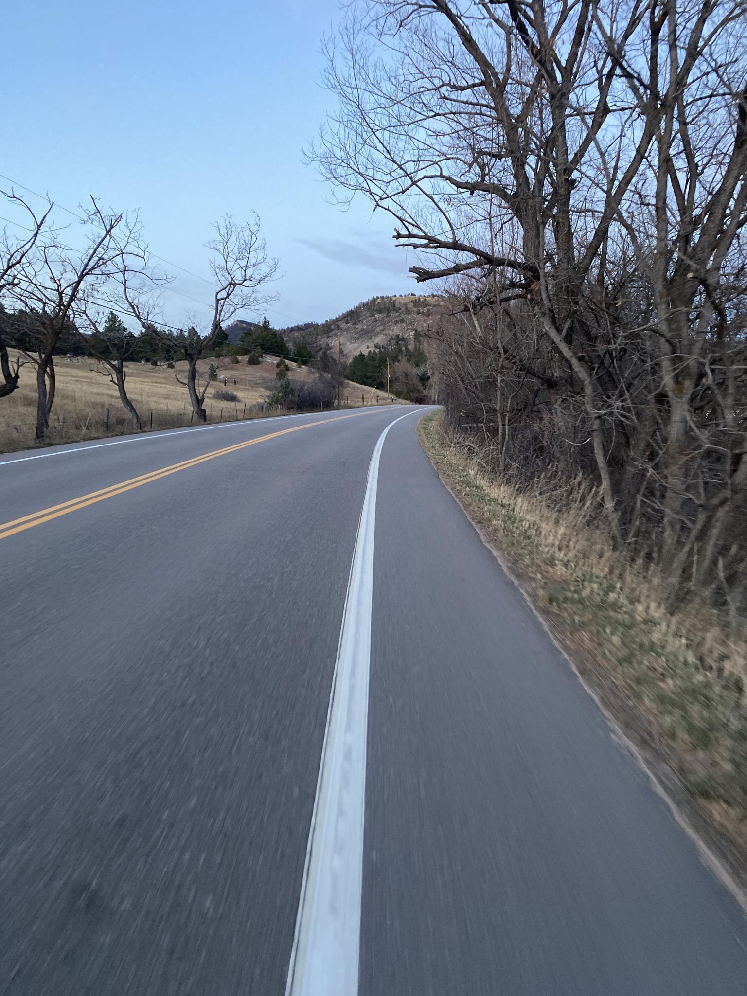 Paved road with a bike lane, bare trees, and hills under a pale sky.