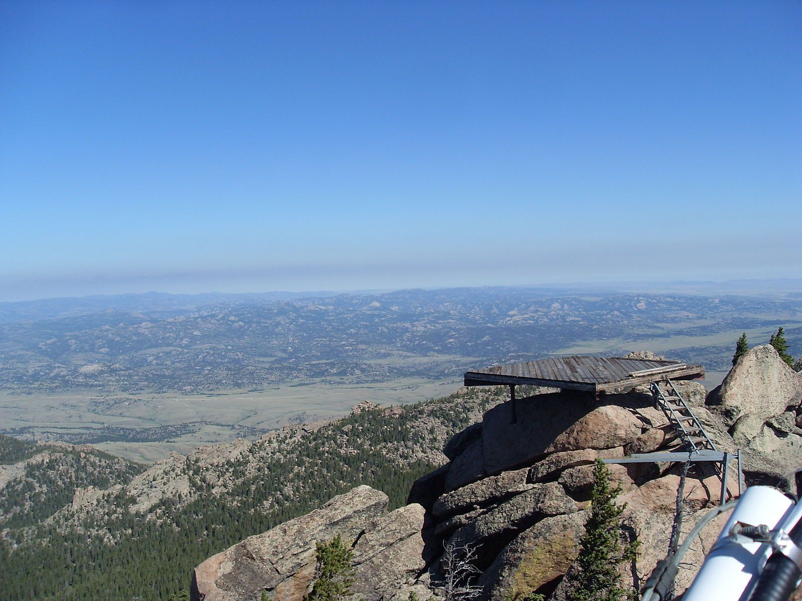 Wooden platform on rocky peak overlooking vast hazy mountain landscape under clear sky. - Laramie Peak Trail