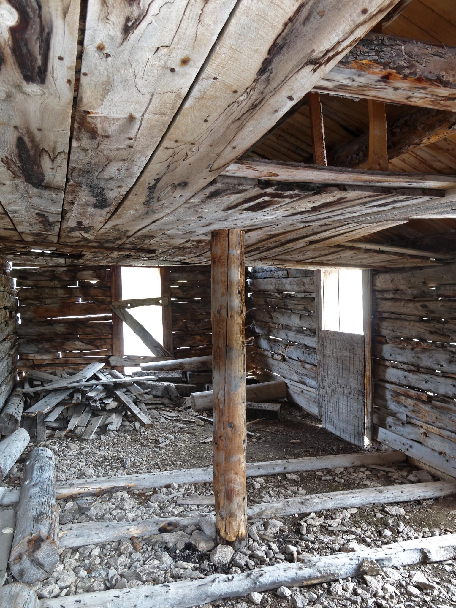 Dilapidated wooden interior with exposed beams, debris, and bright light from openings.