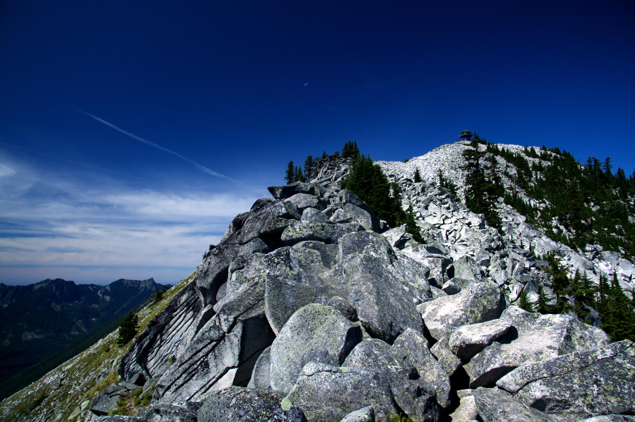 Rocky mountain ridge with sparse trees under a deep blue sky.