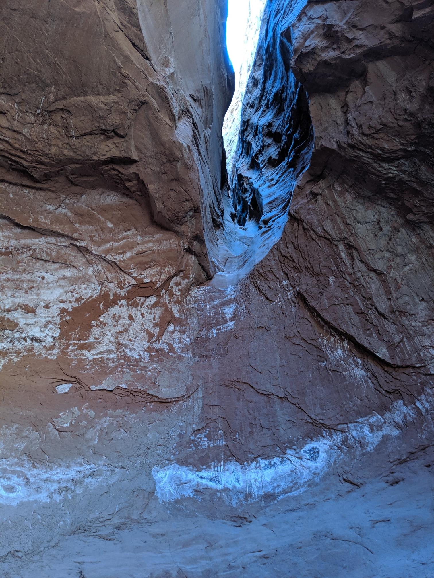 Narrow slot canyon with bright light filtering from above, illuminating rock walls.