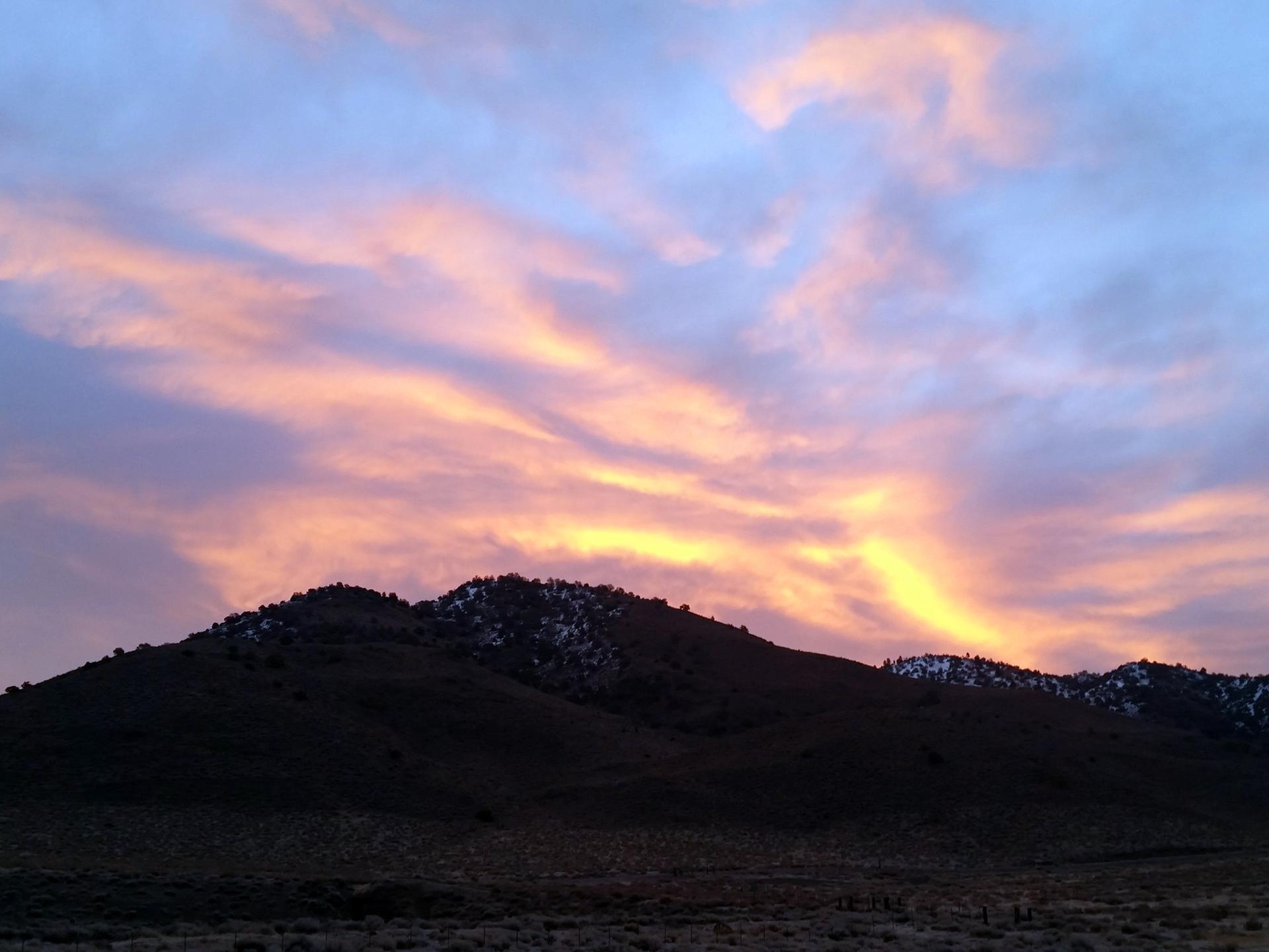 Silhouetted mountains under a dramatic sunset sky with pink and yellow clouds.