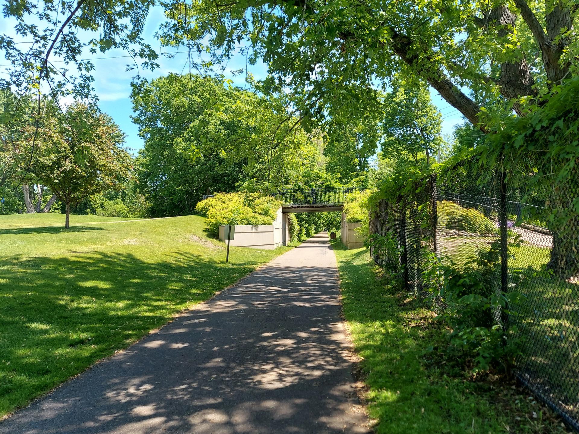 Shady paved path winding through a green park with an archway ahead.