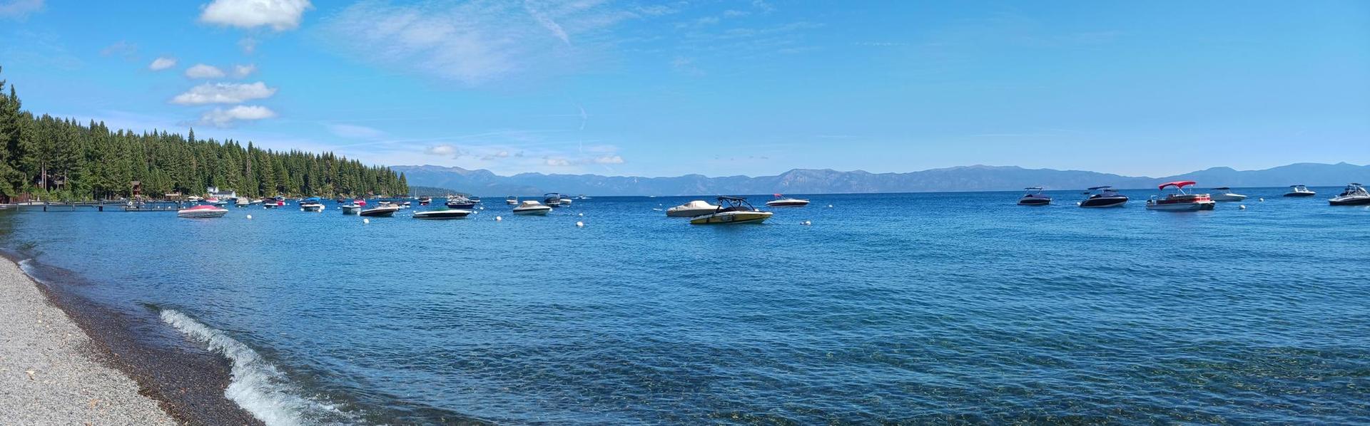 Panoramic view of a blue lake with many boats and a sandy beach.