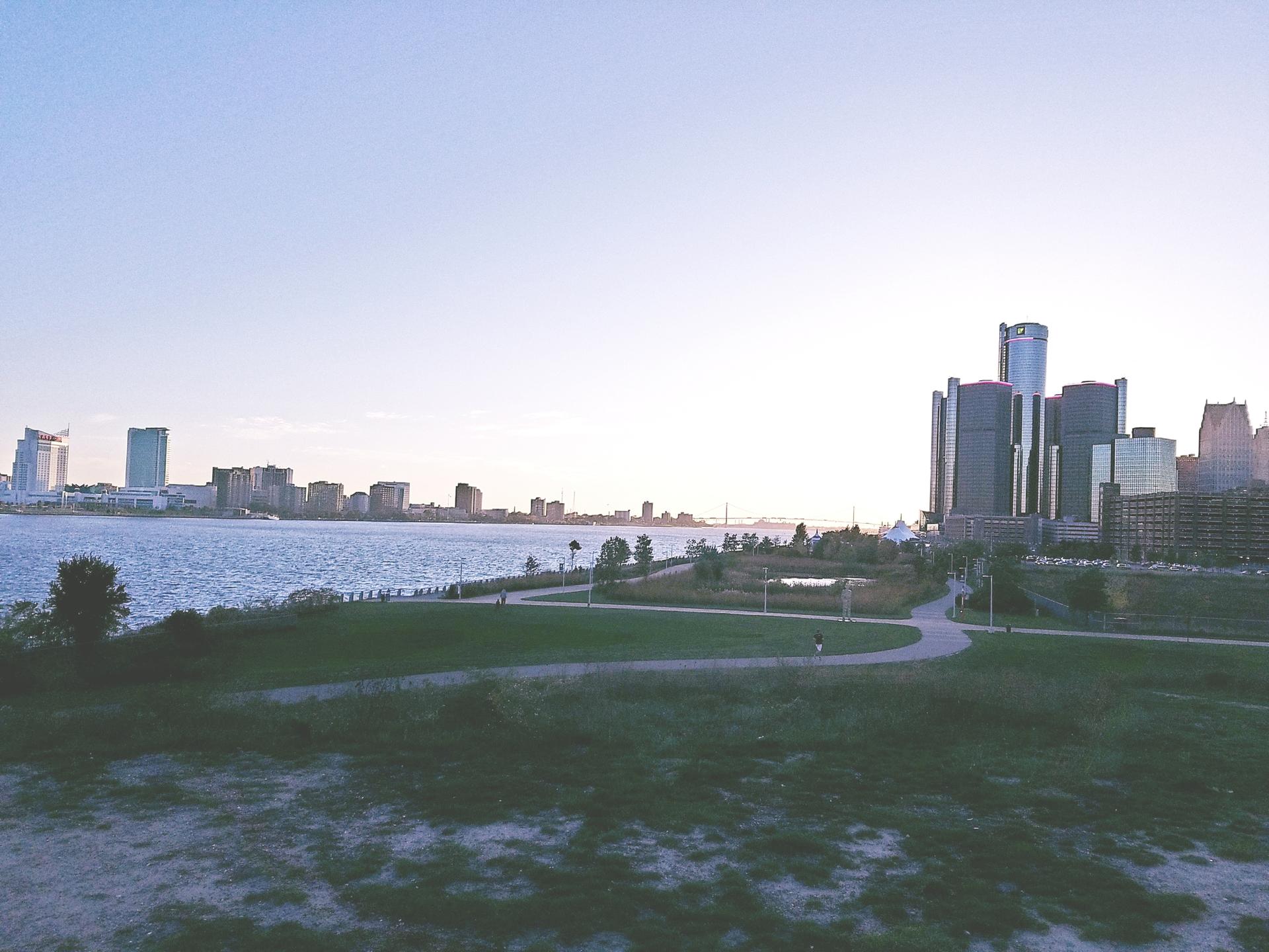 City skyline across calm water, viewed from a grassy park at dawn.