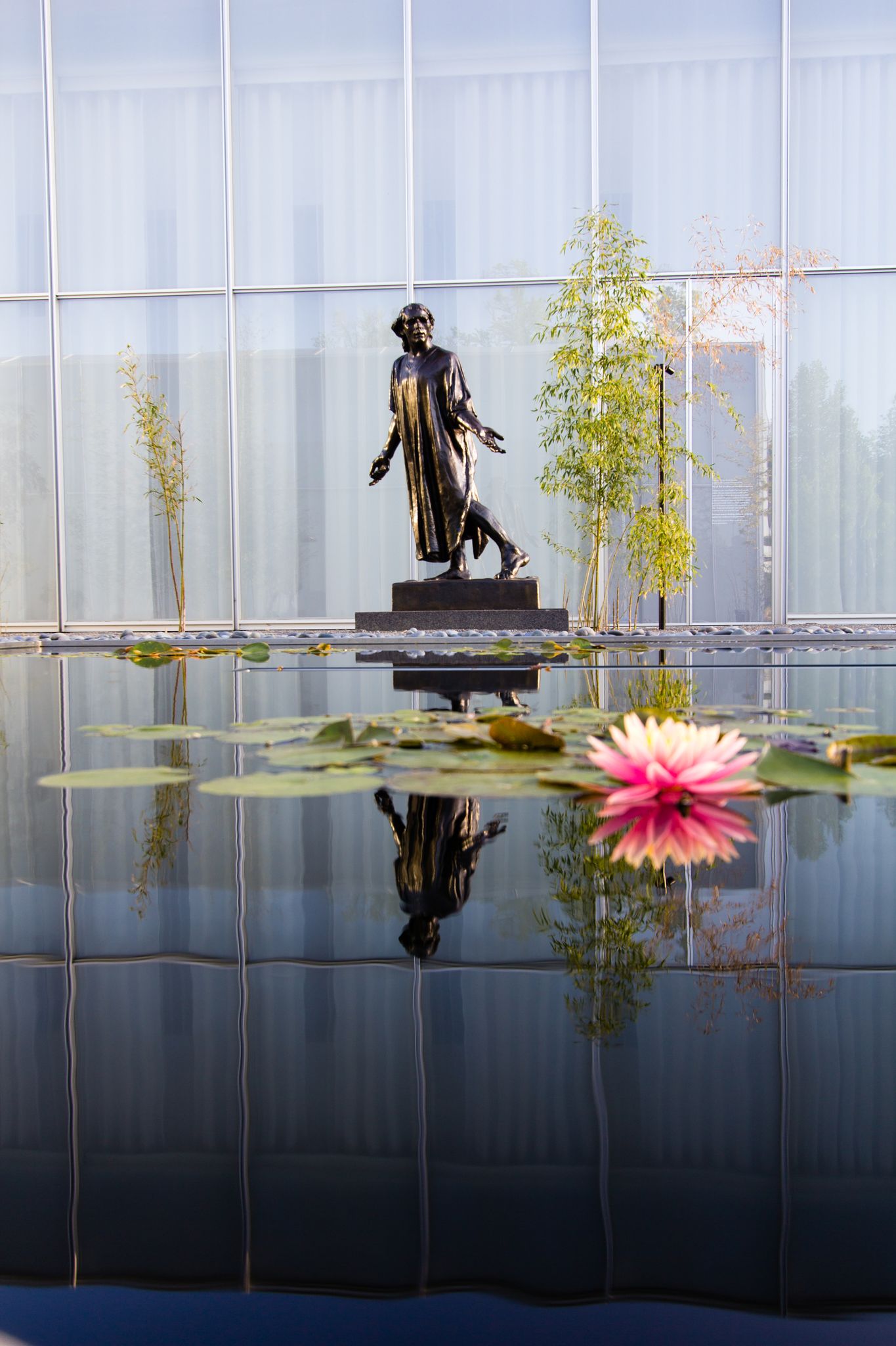 Bronze statue reflected in a pond with a pink water lily, modern building. - Reedy Creek Trail
