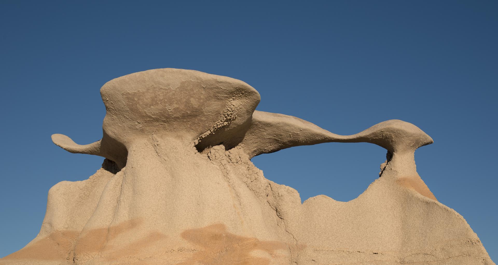 A unique, arch-shaped rock formation stands against a bright blue sky.