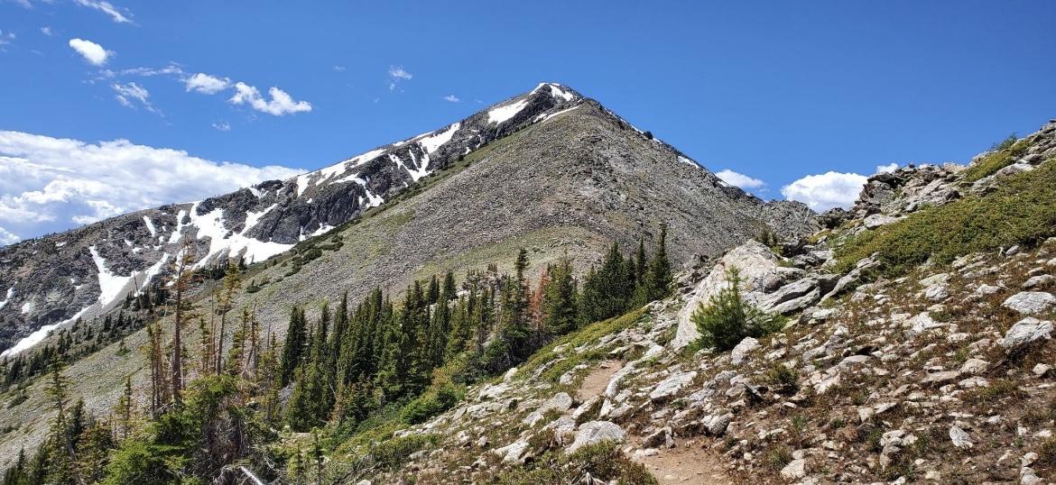 A steep, rocky mountain peak with a winding trail under a clear sky.
