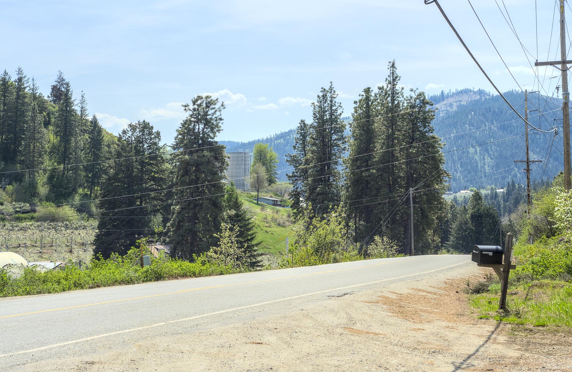 A rural road with a mailbox, power lines, and forested hills under a bright sky.