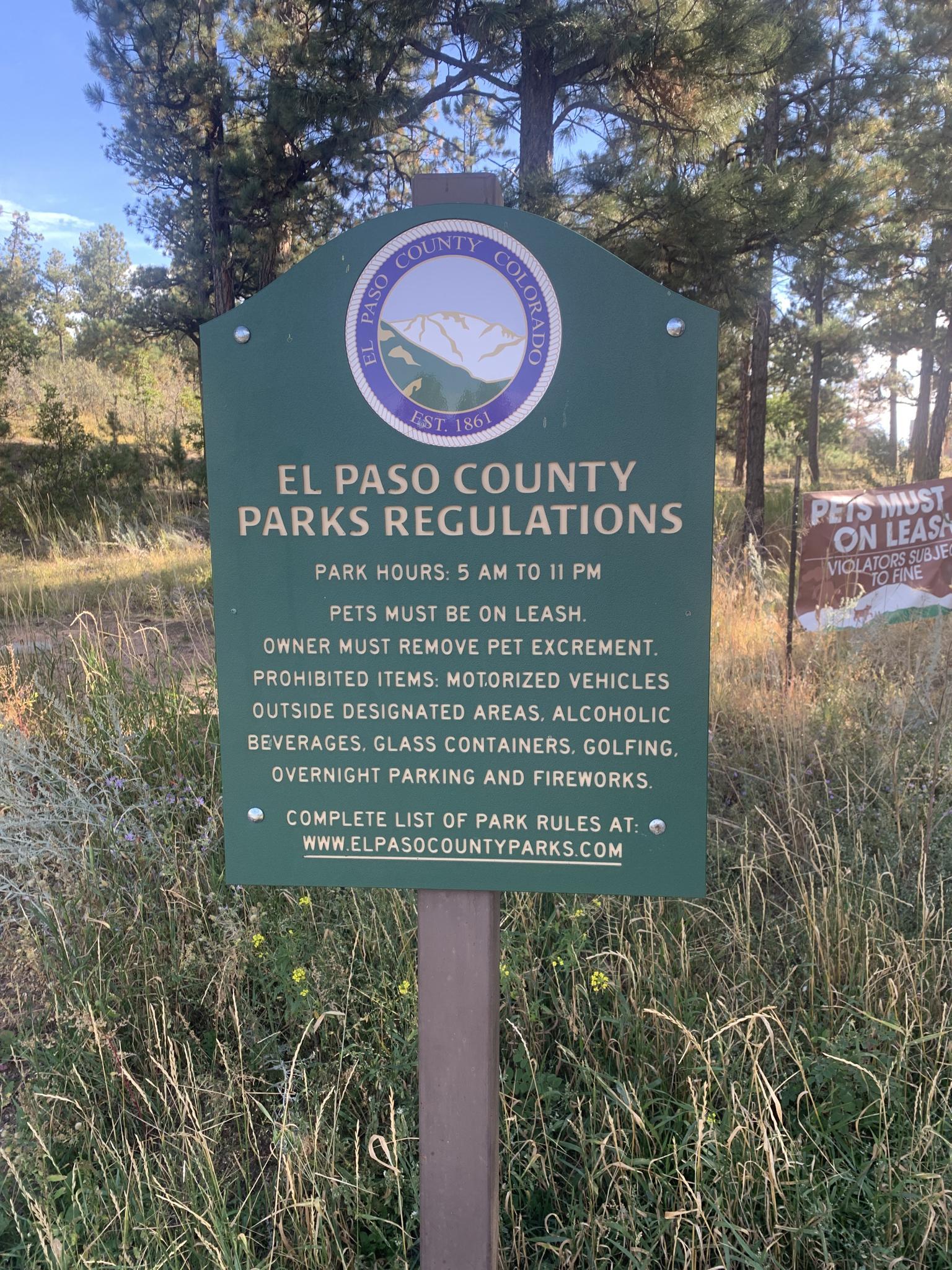 A green park regulations sign stands in tall dry grass.