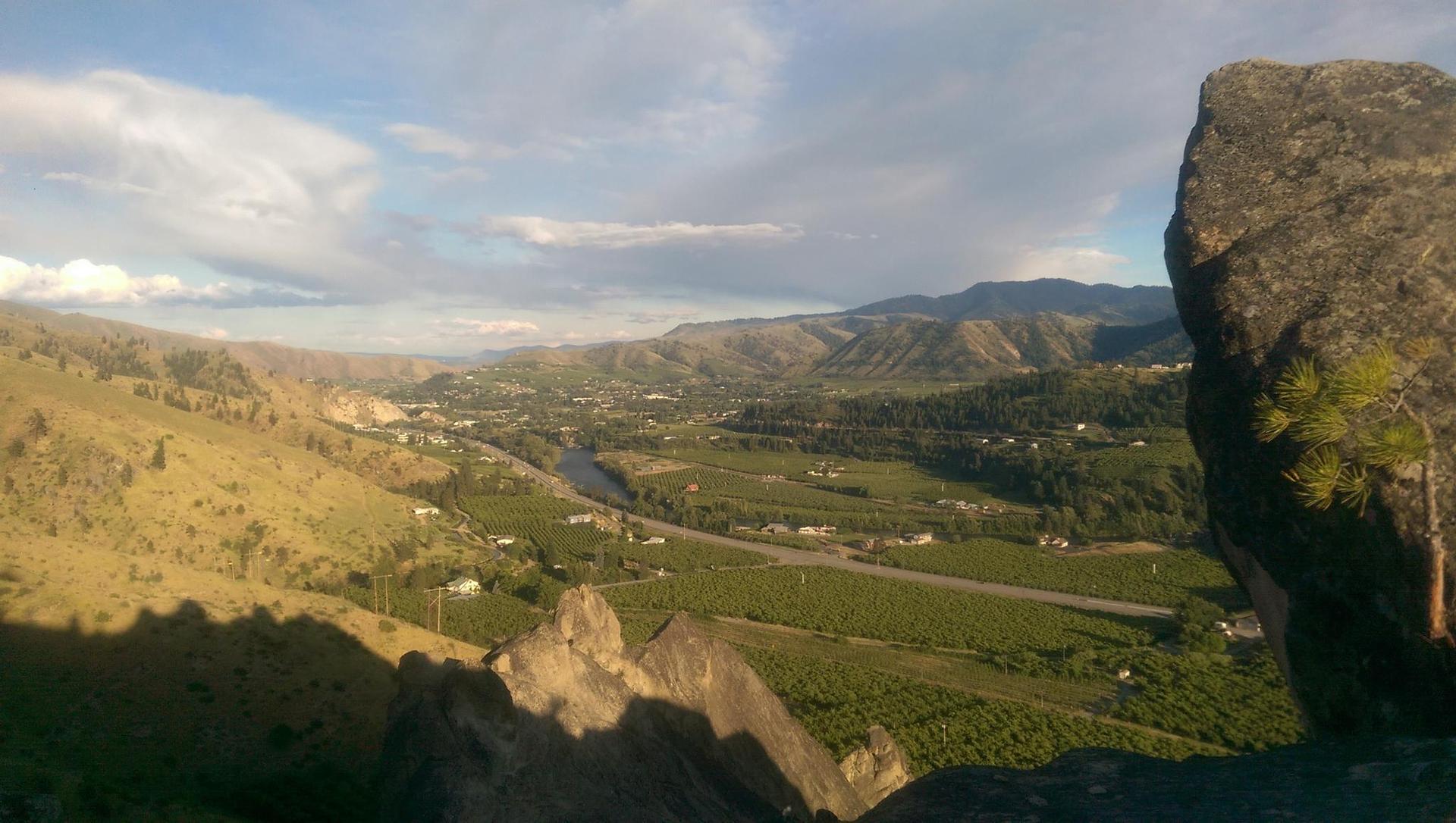 Panoramic valley view with a winding river, agricultural fields, and distant mountains.