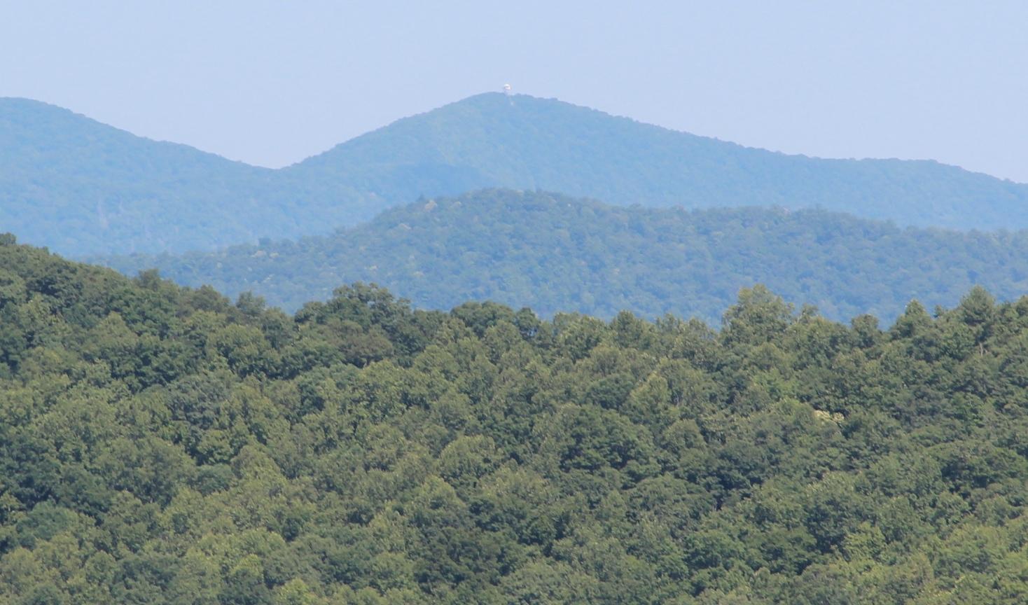Dense green forest covers rolling hills with hazy blue mountains in the background.