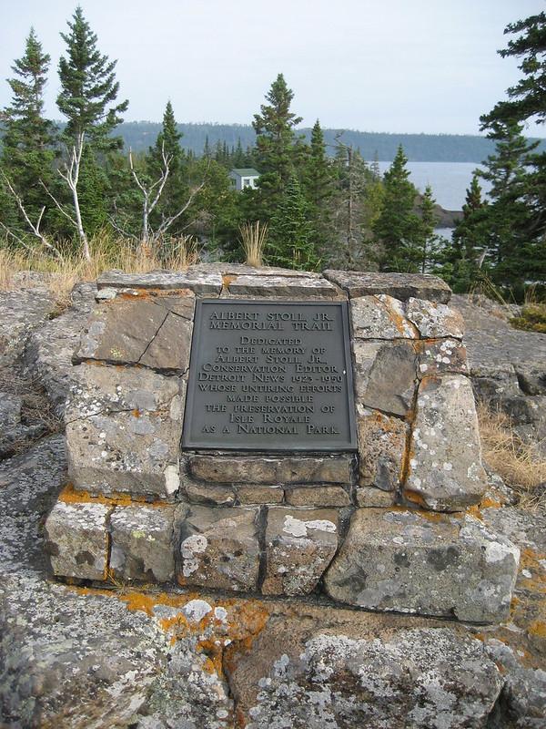 A stone memorial plaque on a rocky outcrop overlooking a body of water.
