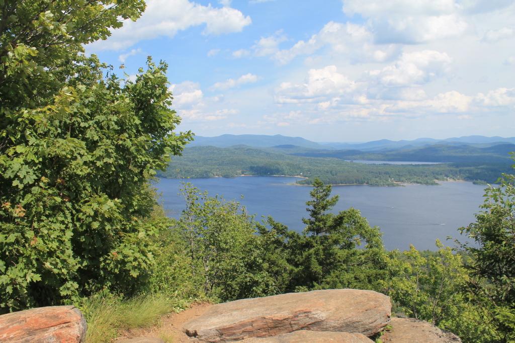 Overlook of a vast lake and distant mountains, framed by green trees and rocks.