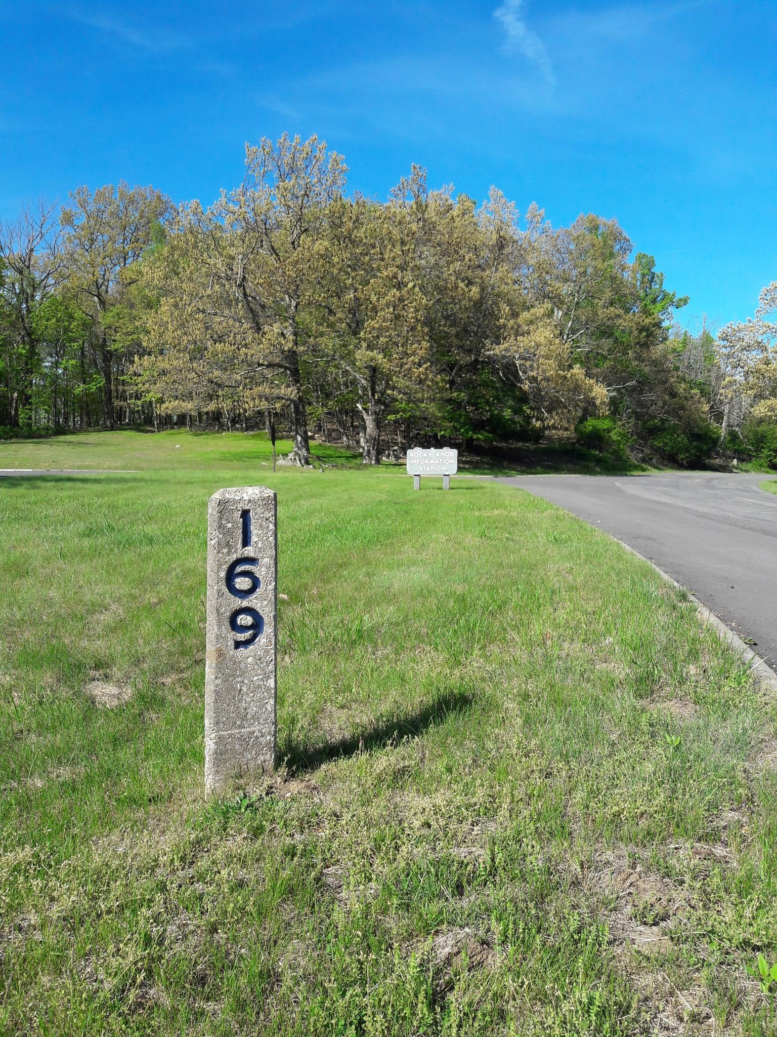 Concrete marker with '169' in a grassy field next to a paved road.