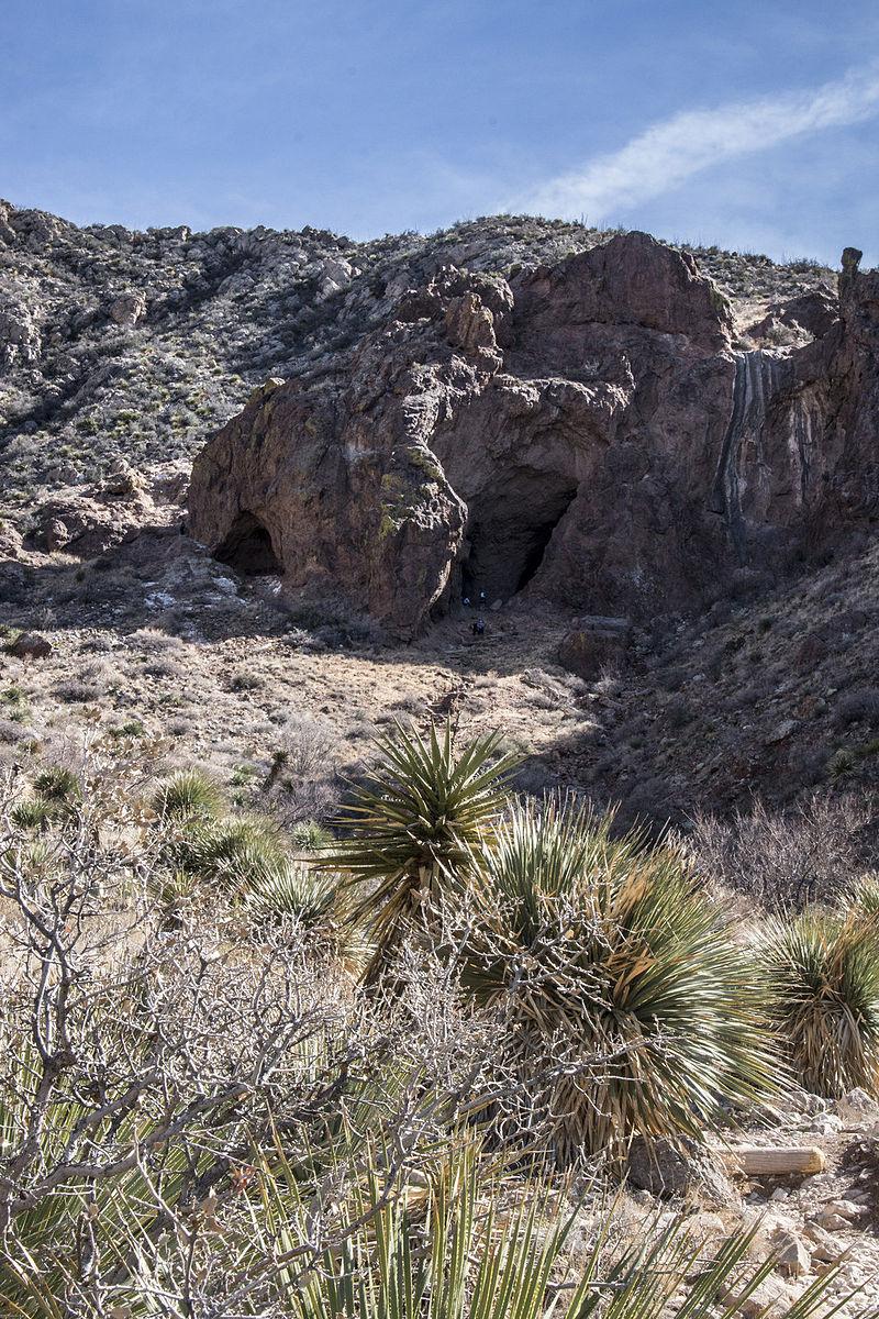 Large rocky formations with cave openings in a sunny desert landscape.