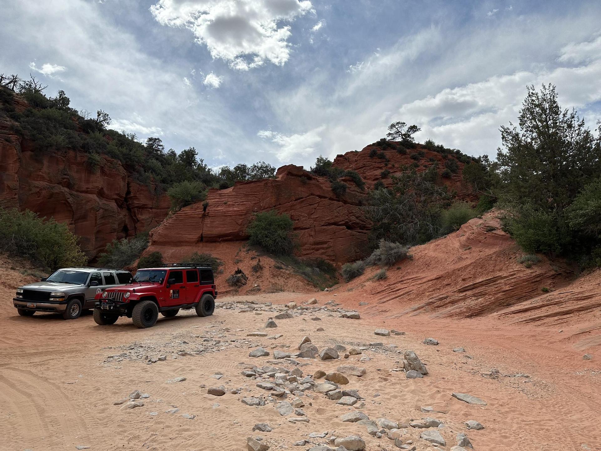 Two off-road vehicles parked on a rocky desert trail near red cliffs.